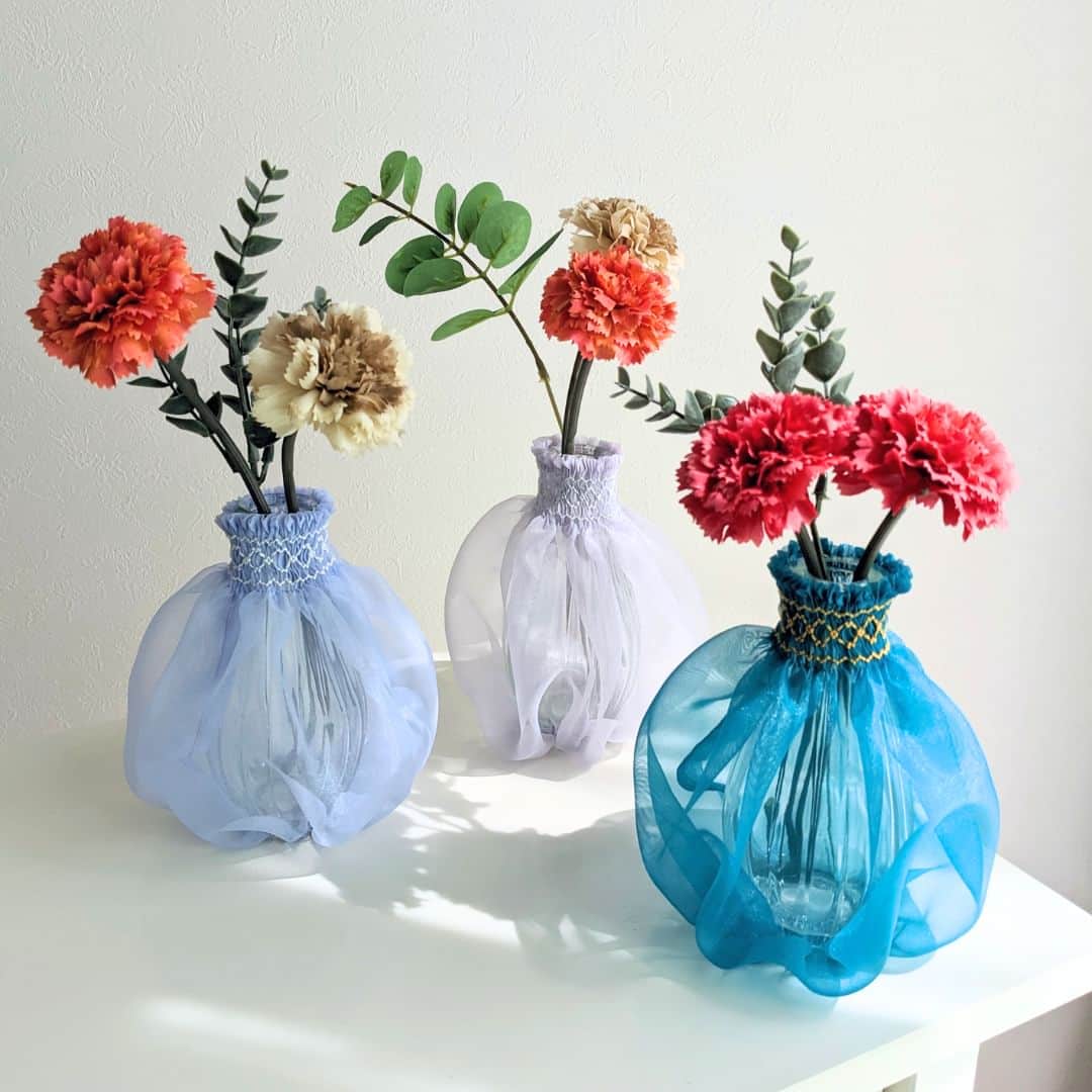 minneさんのインスタグラム写真 - (minneInstagram)「ターコイズブルーが涼しげな花瓶のドレス  ガラスの花瓶とスモッキング刺繍が施されたオーガンジーの透け感がきれいなドレスのセット。 オプションでカーネーションの造花をプラスできるのも嬉しいポイント。お花好きな方や母の日の贈り物にもぴったりです。手持ちの花瓶にドレスを着せても◎  お部屋のアクセントとして存在感のある素敵な一輪挿しを取り入れてみませんか？  ▶️詳細は @minne_official のプロフィールリンクから  ＊ーーーーー  🏠Suicoduki（スイコヅキ）さん（ @suicoduki_handmade ） 「スモッキング刺繍という技法でバッグやポーチ、雑貨などをつくっています。 生み出すひとつひとつの作品を通して、皆さまと心を通わせることができたらとても嬉しいです。」 https://minne.com/ohalico  ＊ーーーーー  🔍花瓶のドレス（ターコイズ） https://minne.com/items/34037721  #花瓶のドレス #オーガンジー #花瓶 #一輪挿し #スモッキング刺繍 #カーネーション #母の日ギフト #母の日 #花好きへのギフト #花瓶カバー #ターコイズブルー #夏のお部屋づくり #夏インテリア #刺繍」5月3日 18時30分 - minne_official