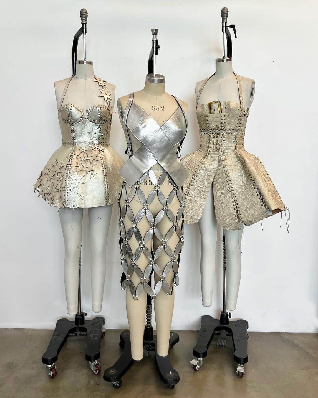 ZANA BAYNEのインスタグラム：「From the Archives 🌹  Left to right:  Spring 2015 Metallic Champagne Leather “Rita” Dress fully riveted together with cascading stars  Spring 2016 Silver Leather “Roxanne Top” in the shape of an X and the “Rio Skirt” with petal shaped links that emulate the same X shape   Fall 2014 Beige Croc Embossed “Buckle Bra” and “Bustle” Dress with brass toned hardware」
