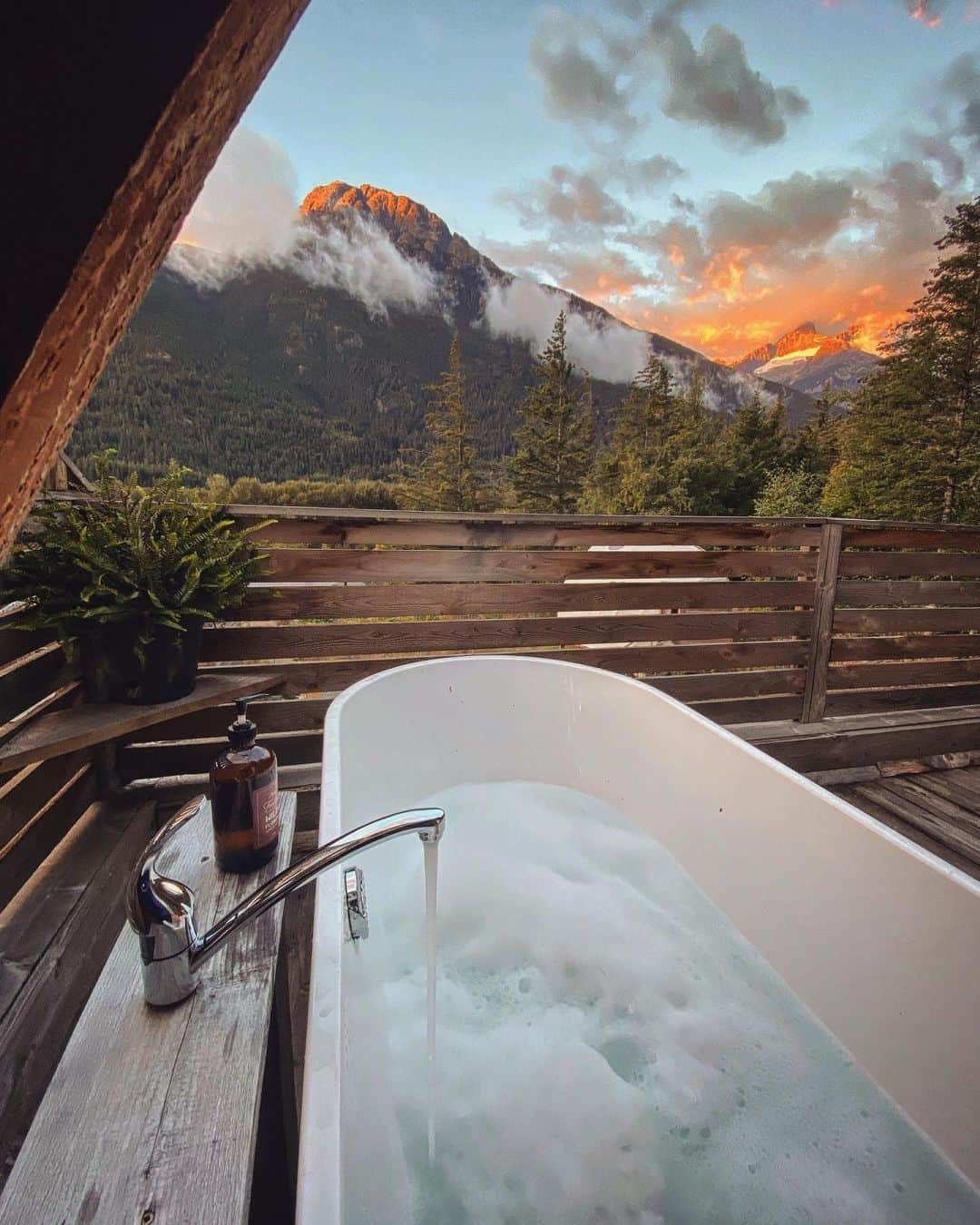 Explore Canadaのインスタグラム：「This is the kind of view we usually see in our dreams! But this one is real life ⛰️  Located in the heart of the Great Bear Rainforest, in traditional Nuxalk Territory, @firvale_wilderness_camp is an all inclusive basecamp for adventure. Or you can choose to lounge in the tub all day, both are good choices 😏  📷: @salking16  📍: @firvale_wilderness_camp, @cariboochilcotincoast, @hellobc   #CCCLives #ExploreBC  [Image description: A large bathtub is filling with water and bubbles. The view from the tub overlooks a forested mountain. The sun casts a deep orange glow from behind the mountain, lighting the clouds.]」