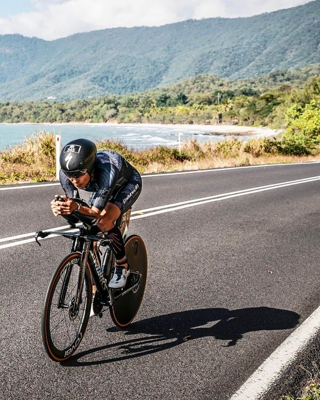 竹谷賢二さんのインスタグラム写真 - (竹谷賢二Instagram)「【2023 #IMケアンズ バイクレポート】 Bike 4:53:56 (ペナルティ5分含む)　1st M50-54  バイクパフォーマンスはエイジカテゴリーならば、ハイパワー領域が低下してきていても常用域は相対的に十二分なので、ランに繋げるペーシングを徹底していくことを重視。 そのためトレーニングも低強度ボリュームを、コナでの合宿を経てクライアントのレベルアップとともに十分な強度で着実に積み上げていくことが出来た。 高強度は各種合宿やレースなどスポットで入れるのみだったが、レース前１ヶ月はレースパワー想定でのペーシング機会をしっかり設けて余裕を持ってコントロールできる状態に。 身体各部の柔軟性向上に取り組んできたこともあり、エアロフォームの改善、エアロアームレストとバイクの新調により、空気抵抗削減も確かめられていたこともありNP210wで、前回2019年の4時間47分 Ave37.3kph NP239w 同等を狙えると予測、果たして例年よりも向かい風が厳しくなかったことにより実走行では達成、タイム的にはドラフティングペナルティ5分加算ではあるが。  T1 Transition 3:45 は軽快に通過、#コンプレスポーツ R2エアロカーフはウエット下に着用していたので、ウエット脱いでシューズを持って走りバイク近くで履きエアロヘルメット被り、#ガーミン #エッジ840 を起動させるのみのシンプルトランジット。  走り出しからペーシングを徹底、上り坂ではパワー上がりがちだか、心拍数を低く抑える意識でトルクを抜いた優しいペダリングで負担をかけずにスピードを乗せていく。 スイムアップが早いと、空いていて全体的にバイクが少ないので追い越しで無駄に加速することがなくなり、圧倒的に走りやすい。 ノロノロ走る休日の高速道路を追い越しして前に出るのと、ガラガラの深夜をマイペースで走るのでは、どちらが一定速度で走りやすいかは誰もが分かるほど明確に違うが、まさにそれ。 加減速が少なければ同じ平均パワーでも平均スピードはあがる、まさにエコ運転で早く目的地に到達できるのだ。  数名速いアスリートに抜かれていくが気にせず自分の余裕感を優先しながらマイペースでクルージング、それでも徐々に追い抜く割合が増えてきて順位が上がっていく。 コースは基本同じだが、折り返しなどが変わっていて、道が狭く荒れたところを通るので以前よりも若干ロスタイムだっただろう。パンク、落車などには十二分に気をつけ安全マージンもしっかり確保し、周りの景色も楽しむ余裕を持って、初めて高台のレックスルックアウト近辺などで煌めく海やビーチ、遠くの島などをはっきりと眺めた。  １度目の折り返しで余裕はあるがいまいち平均速度が高くないことが気になり、抜いていった４〜５台のドラフティンググループに上りで追いつき下りで追い越す#GUエナジー、ドリンクミックス２.５包、リキッド５個、チュウ３袋のほぼほぼ摂れたので1,500kcal確保出来た。1時間あたり300kcalと想定通り。味変に干し梅を少量追加。 #SHIV ハードレーション1,000cc フロント #XLAB 750cc リキッド300cc とおよそ２リットルの水分を摂りつつも、後半エイドでプラス補水。  １周目往路追い風1時間、復路向かい風1時間、２周回目往路追い風1時間と刻み、ケアンズ市内に戻る復路の追い風2時間が勝負所で、3時間余裕を持って進んできても、やはりジワジワ数ワット微妙に低下してしまう。  パームコーヴ手前から工事区間と分岐点の狭い区間で序盤に追い抜いたドラフティング集団に追いつかれてしまい、追い越されていく。 台数数えながら一台一台ゆっくりと後ろに下がっていくが、ここでドラフティングを取られてしまう。どうやらこの集団をマーシャルはチェックしていたようで、ペダリングしながら後ろに下がっていて距離が詰まっていたのでその瞬間を判断されたよう。 ここで何を言っても仕方ないので、ペナルティボックスがT2の前にあることだけ確認して、スイムのタイムが帳消しになっただけだと気持ち切り替える。  こうなったら利用させてもらおうとその集団にきっちり距離をとって追従、どうやら４人いる中でドラフティングしているのは2人だけで、他の2人は先頭交代しながらも距離感は適切。後ろで見ているとよくわかる。 向かい風なのでうっかりすると距離縮めてしまうので慎重に気をつけながら追従していると、１７０kmくらいのもう市内間近の車並走区間で、マーシャルが抜いていく。最後までチェックしていたようで、とりわけドラフティングは酷かった一人をブルーカードを出していたので、胸がすく思いがした笑  ペナルティボックスでその彼と無言の５分間、ストレッチを入念にしてランに備える。  Garmin Connectで マルチスポーツ アクティビティをチェックしてください #beatyesterday https://connect.garmin.com/modern/activity/11368447052  #トライアスロン #レース #アイアンマン #IRONMAN #バイク #スペシャライズド #ガーミン #ラリー #フーブ #スペシャライズド幕張 #エンデュアライフ」6月23日 13時26分 - tktakeyakenji