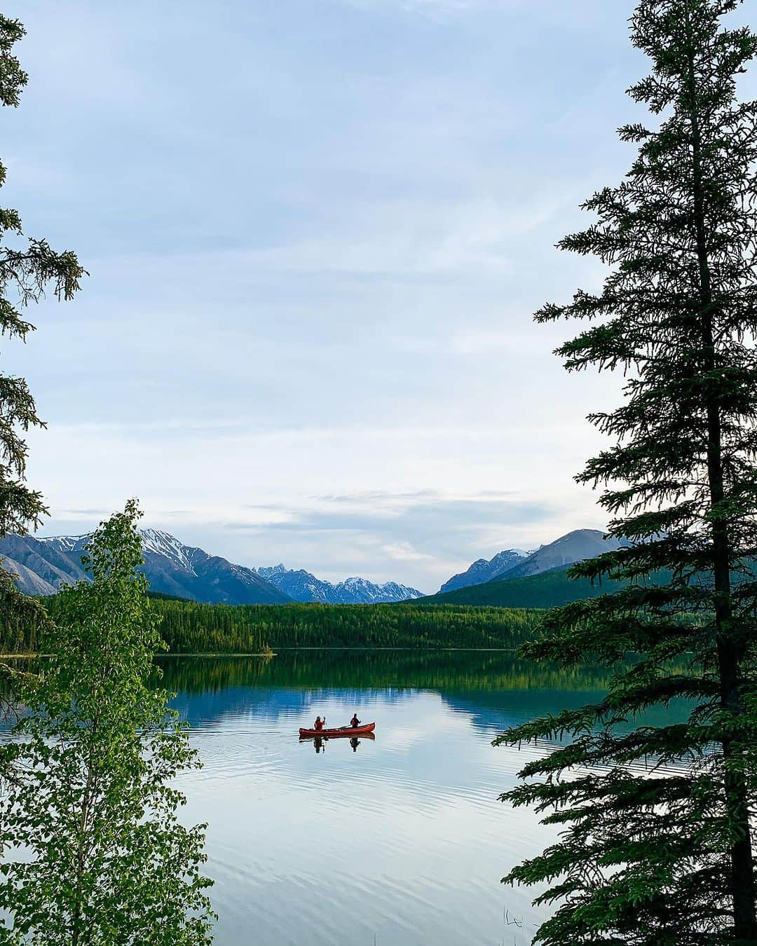 Explore Canadaのインスタグラム：「Looking for your next adventure? 🛶  Nahanni National Park Reserve encompasses 30,000 square kilometers of the Northwest Territories and is a designated UNESCO world heritage site.   📷: @alyssaetsell  📍: Nahanni National Park Reserve, @spectacularnwt   #SpectacularNWT  [Image description: Two people are pictured in a canoe in the middle of a blue lake. Trees frame the foreground, and snow-capped mountains stand in the distance.]」