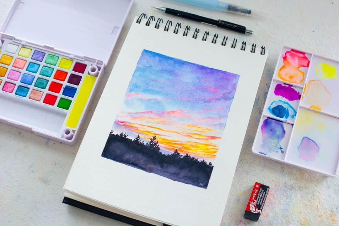 Sakura of America（サクラクレパス）のインスタグラム：「Hi everyone! I’m Octavia Spriggs, a watercolor artist from West Virginia. I’m so excited to be guest posting with Sakura. I’ll be sharing some tips about using Koi watercolors with you!  🌅 I used the Koi Creative Art Colors Pocket Field Sketch Box to paint a sunset landscape that I photographed from my back porch.  ✨The neon pigments in the #sakurakoi Creative Art Colors box are perfect to capture the vibrancy you’ll see right before the sun sets over the horizon. I used a black Koi Watercolor Brush Pen to quickly sketch out the treetop silhouettes and then blended that with a wet paintbrush to fill out the bottom of the painting.  I’ll be back soon with a few more posts! You can see more of my work at @octaviaspriggsstudio 💛」