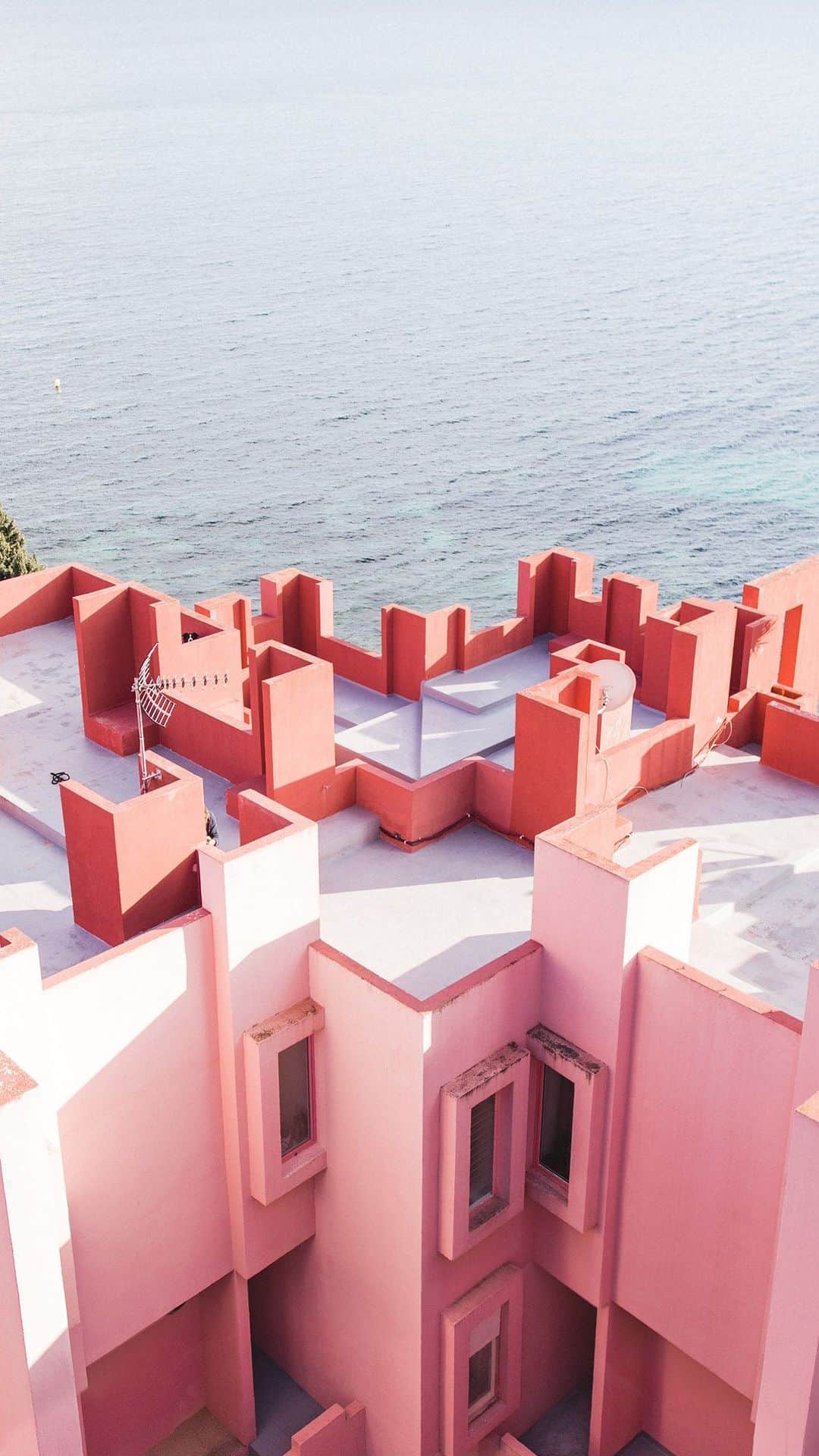 Andrew Knappのインスタグラム：「This was meant to be a reminder that my print of Muralla Roja is available until Friday only. And then I remembered that today would have been Momo’s birthday. And then this became fitting because it was definitely on the list of favourite places I explored with him.   My friend @helananas told me about Muralla Roja, a real life M.C. Escher drawing in Spain by architect Ricardo Bofill, which sounded impossible. A place I’d likely never see in my life, so I forgot about it. A few years later, I found myself exploring this building in complete awe with Momo by my side. It still feels like we visited another planet.」