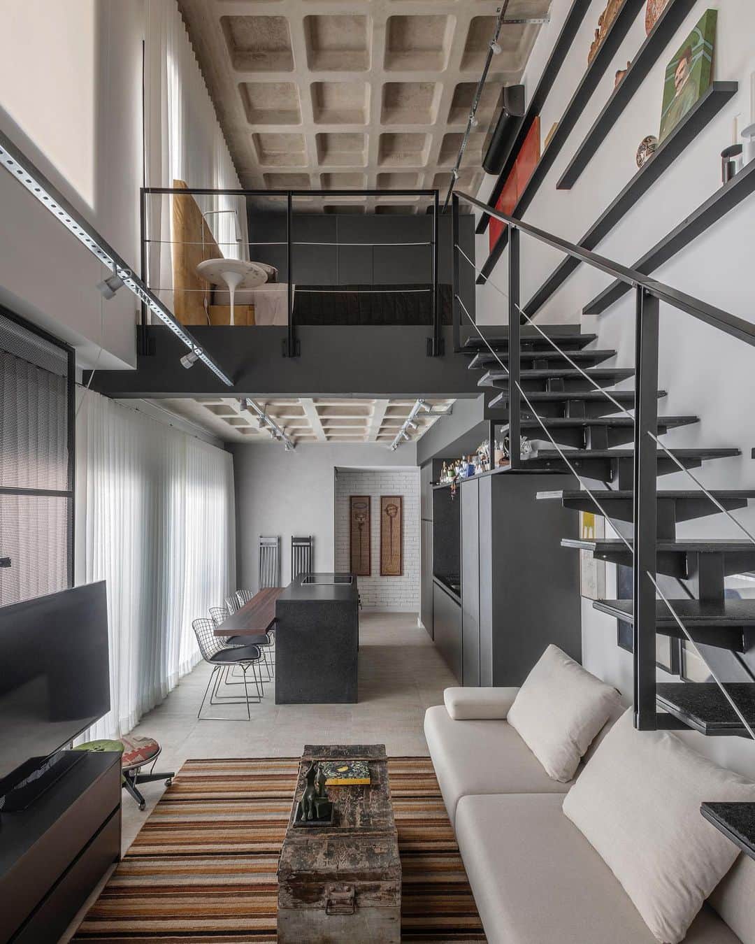 のインスタグラム：「Localizado em Belo Horizonte (MG), este apartamento duplex de 64m² foi transformado em um refúgio de férias e espaço de exposição de arte. Com a ajuda do arquiteto Júnior Piacesi, do escritório (@piacesiarquitetura), o projeto se concentrou em soluções de marcenaria para otimizar os pequenos espaços, sem demolir paredes.  A estética industrial, baseada em tons sóbrios, foi complementada com móveis e obras de arte pessoais, resultando em um ambiente contemporâneo e acolhedor. O destaque vai para a cabeceira estofada com lona antiga trazida da Bahia. Uma combinação perfeita de funcionalidade e estilo para as férias na capital mineira.  📸 @estudiony18」