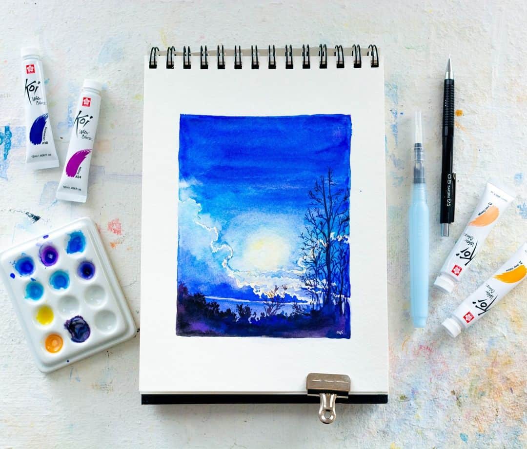 Sakura of America（サクラクレパス）のインスタグラム：「🌙 Today, I painted a moonrise using Sakura Koi Watercolor tubes. I loved the #sakurakoi tubes for this scene because of their rich pigmentation. Summer is a perfect time to take a twilight walk and watch the stars come out.  🌲 After beginning with a 0.5 Sakura mechanical pencil, I painted the light coming from around the moon using Pale Orange with Deep Yellow. The sky fades from Cerulean Blue to Ultramarine.  ✨I then added in the glow around the clouds, followed by the darker cloud shadows once that glow had dried. I then mixed Ultramarine, Purple and Ivory Black to create the treetop silhouettes.   Have you ever tried a painting of the night sky? I’m always surprised at how many colors I can pull out of the dark. @octaviaspriggsstudio」