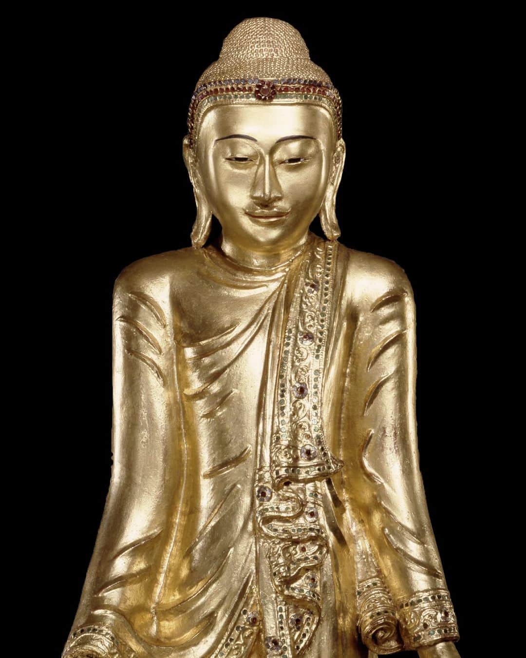 大英博物館のインスタグラム：「Between the 16th and the 19th centuries, the wealth and power of the kingdoms in central Myanmar grew as its courts twice expanded into huge mainland Southeast Asian empires.   In keeping with changes occurring across the Buddhist world during the 19th century, Burmese Buddha images like this one became more naturalistic looking.  In addition to the standard seated pose, Buddha images were also produced in standing and reclining postures to reflect the various events of the historical Buddha’s life.   This figure, with its elegantly folded robes edged with glass inlays, offers the devotee a medicinal fruit as a cure for spiritual woes.  Learn more in our exhibition highlights – link in bio.   Supported by Zemen Paulos and Jack Ryan  🔎 Standing Buddha image offering a medicinal myrobalan fruit. Wood, lacquer, gold and glass, present-day Myanmar, late 19th century.  #BritishMuseum #BurmaToMyanmar」