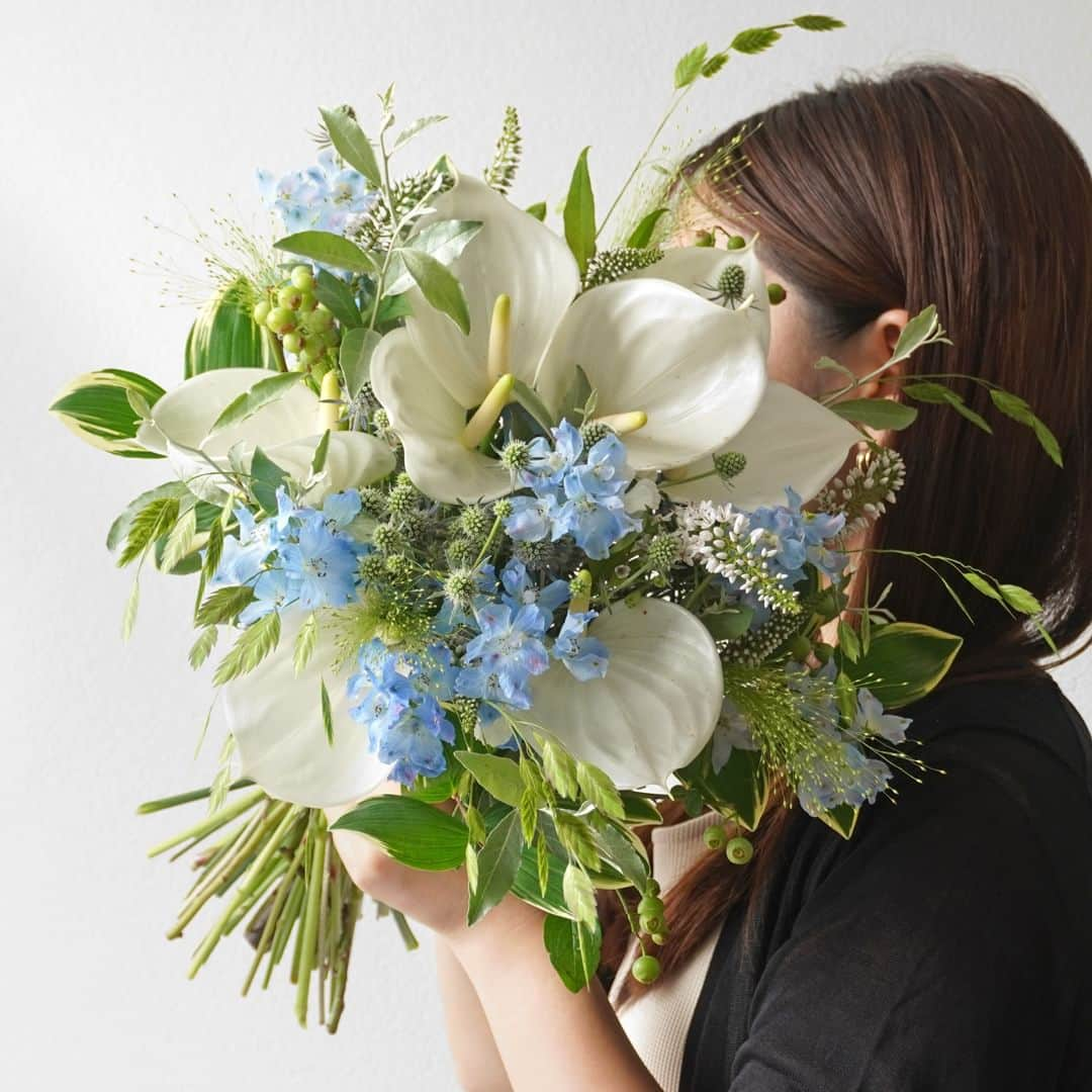 AOYAMA_HANAMOのインスタグラム：「夏を涼しげに彩る、白とブルーの花々。 ・ 純白のアンスリウムに涼しげな淡いブルーのデルフィニウム、グリーンのエリンジュームなどを合わせた夏のブーケ。細やかで美しい穂をもつスモークグラスや、柔らかな曲線のグリーンスケール、ふっくらと丸いブルーベリーの実などがナチュラルで軽やかな雰囲気を演出しています。 - - - #aoyamahanamo #青山花茂 #お花のある生活 #花が好きな人と繋がりたい #花を飾ろう #花のある暮らし #花のあるくらし #花のある日常 #癒しの花 #季節の花 #旬の花 #花とおうち時間 #花贈り #フラワーギフト #花の贈り物 #アンスリウム #リシマキア #デルフィニウム #ブルーベリー #ロシアンオリーブ #スモークグラス #グリーンスケール #ナルコユリ #エリンジューム #ブーケ #ナチュラルブーケ #クラッチブーケ #夏の花 #夏の花束 #夏のブーケ」