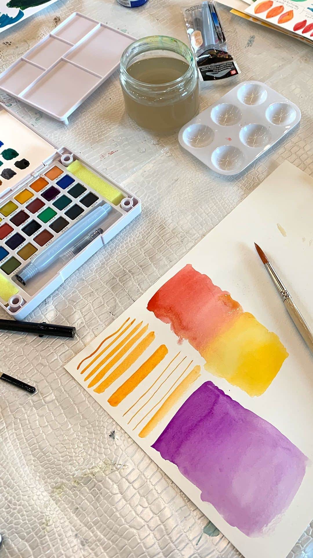 Sakura of America（サクラクレパス）のインスタグラム：「Hi it’s Jeanetta again of @nettdesigns and I am here to share with you how I taught my watercolor workshop at my art retreat in France using the Koi Water Color kit. If you saw my previous post, you know that I prepped some examples for this lesson. I taught them watercolor basics starting off with making gradient washes and then making curves and lines of different widths and waviness. I wanted them to get used to moving the paint in different ways and see how the paint reacts to the amount of water they use. Then they could take the methods and create circles, other shapes and words.   A good watercolor wash is made by using a wet brush dipped into watercolor and moving it around your paper. Adding more water can enable the paint to bleed and spread out into a larger area. It can be used for creating backgrounds, making a sky, filling in shapes and so much more. Dab other colors into the wet areas using your brush, creating a wet-on-wet technique that gives it a lot of texture and blends the colors in such gorgeous ways.」