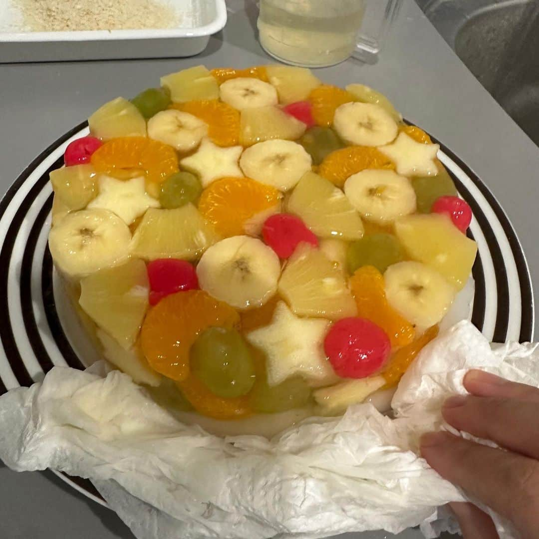 山本ゆりさんのインスタグラム写真 - (山本ゆりInstagram)「誕生日や人が集まる時にオススメ ⁡ 【宝石箱ゼリーケーキ】(命名:アミ)   この時期、うちの子にはスポンジケーキよりゼリーや果物が喜ばれるのと、作るのもゼリーのほうが圧倒的にラクなんで、両者の利害一致で最近の夏の誕生日はもっぱらゼリーにしてます。   下の層はカルピスゼリーですが、無くても全然いい！いちごが季節的に無いので缶詰のさくらんぼで色を添えました。 ⁡ 果物ギッシリ詰めてるから、果物が沈まないように時間差で層ごとに固めて流して…とかせんでもいいし、ロウソクも刺せます。 ⁡ しっかり硬めの配合にしてるんで切りやすいし、固まらないとかもない！手間の割に見栄えがするんで是非作ってみてください。 ⁡ ------------------ ⁡ 材料(18㎝のケーキ型1個分)※底が抜ける型はNG  ⁡ ・バナナ…1本 ・りんご…1/2個(一部あまる) ・皮ごと食べられるマスカット…1房 ・みかんの缶詰…大1缶(約425g　固形量約235g)　※缶汁も使います ・缶詰のパイナップル…5枚　※缶汁も使います ・缶詰のさくらんぼ…6粒ぐらい ・粉ゼラチン…5g×2袋 ＜二段目＞ ・カルピス(原液)…150ml ・水…300ml ・粉ゼラチン…5g×2袋   ※果物は好みのものを合計800gぐらい。キウイ、メロン、スイカ、生のパイナップルやマンゴー、イチジクなどはたんぱく質を分解する酵素が入っててゼラチンが固まらないので注意！   ＜作り方＞ ①耐熱ボウルにみかんの缶汁200mlを入れ、粉ゼラチン2袋を振り入れて混ぜ、2分ほど放置してふやかす。(残りの缶汁も使います)   ②パイナップルは食べやすく切り、さくらんぼは爪楊枝で種をとる。ブドウは好みで半分に切り、りんごは7ミリ厚さに切ってから型で抜き、バナナは輪切りにする。型に②の果物を詰める。   ★バナナとりんごは変色するんで最後に切ってください。ゼリー内では空気に触れないんで大丈夫です！ ⁡ ★まずは底や周辺が良い感じに見えるよう、果物がかぶらんように詰め、型抜きしたりんごも周囲に散らしてから、残りの果物を上に詰めていくのがオススメです。 ⁡ ③  ①のボウルを電子レンジ(600W)で1分30秒ほど加熱して完全に溶かし、残りの缶汁200mに混ぜ(缶汁200mlも残ってない場合は水を足して下さい。私も足してます！チンしたものと合わせて合計450mlぐらいになればOK)、型に流して冷蔵庫で３時間以上しっかり冷やし固める。 ⁡ 余力があれば… ⁡ ④カルピスゼリーを作る。水50ml(分量外)を耐熱性の器(茶碗などでも)にいれ、粉ゼラチン2袋をふりいれて混ぜて2分ほどふやかし、レンジで30～ほど加熱して完全に溶かす。分量の300mlの水とカルピス原液を混ぜ合わせたところに今のゼラチン液を混ぜ合わせ、冷めたら④の上に静かに流して冷蔵庫で2時間以上冷やし固める。 ⁡ ★温かいうちに流すと下の段と混ざるんで注意！ ⁡ ★上まで流しすぎたら運ぶときにこぼれるんで注意！（私はパンパンで冷凍庫いれたら扉閉めるときに揺れてザバーと流れてた)   ⑤しっかり固まったらフライパンなど底が全部浸る容器に熱湯を張り、底を5～10秒つけてちょっとだけ溶かし、お皿を逆さまにかぶせてホッと逆さまにする。上から押さえて前後に小刻みに揺らして型からはずす。(プリンを型から出す時と同じで、上下じゃなく横に振動させるとカポッととれます） ⁡ 完成‼️ ⁡ ★と言いつつ、溶かし過ぎてお皿がゼリー液まみれになってペーパータオルで吸い取りました。(8枚目参照) ⁡ ------------------ ⁡  #レシピ #簡単レシピ #おうちごはん #料理 #レンジレシピ  #お菓子 #お菓子作り #簡単おやつ #ゼリー #誕生日 #誕生日ケーキ #ゼリーケーキ #誕生日レシピ #カルピス　 ⁡ 最後は腰の動きが独特なダイチ　(服は母が持ってきてくれたイチゴ食べまくって汚れた)」7月1日 19時02分 - yamamoto0507