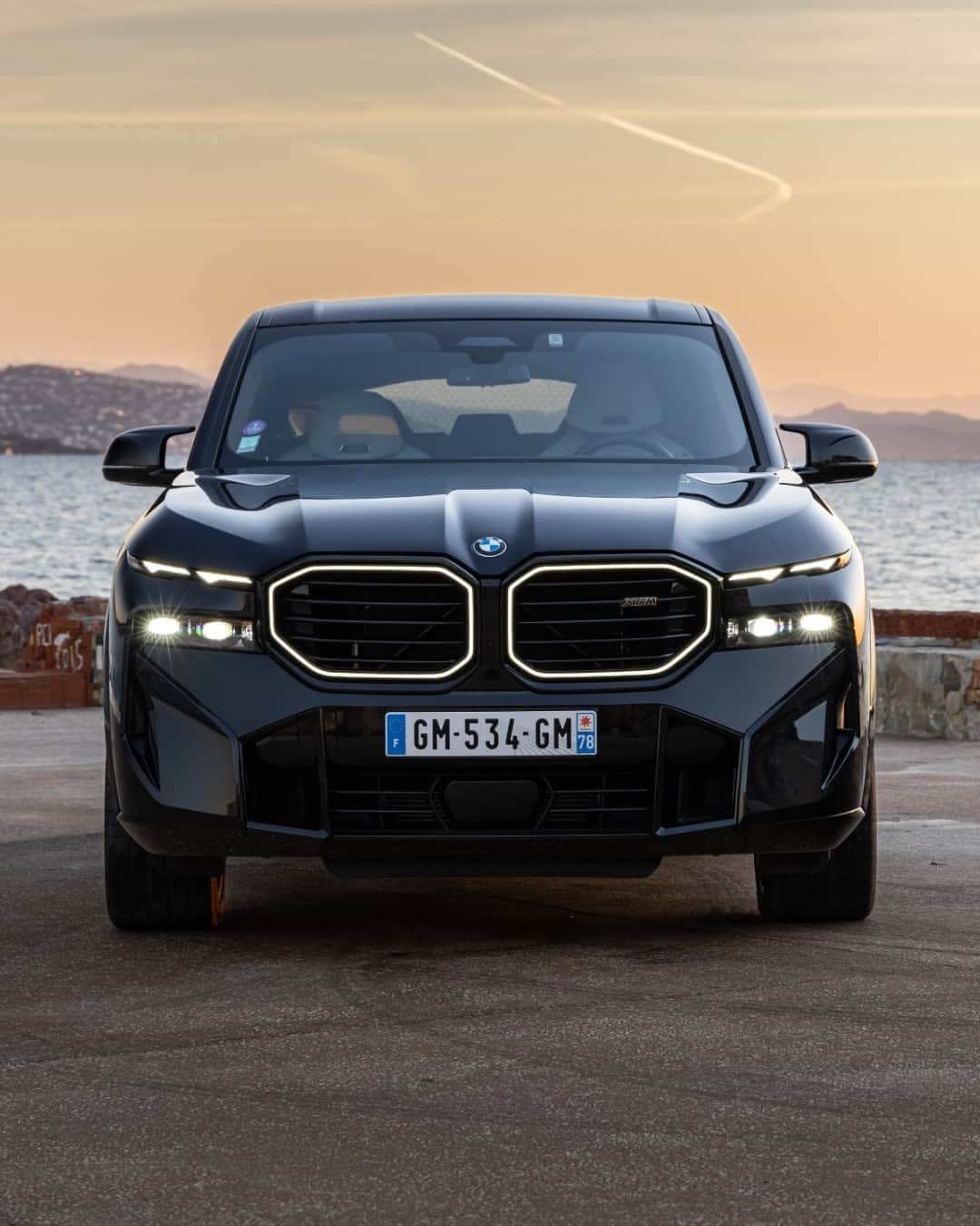 BMWのインスタグラム：「Sea-bound stance and sophistication 🖤 The BMW XM . #BMWXM #BMW #BMWM #MHybrid #MPower __ BMW XM : Combined fuel consumption, weighted: 1.6–1.4 l/100 km. Combined power consumption, weighted: 35.8–32.9 kWh/100 km. Combined CO2 emissions, weighted: 36–32 g/km. All data according to WLTP. Further info: www.bmw.com/disclaimer」