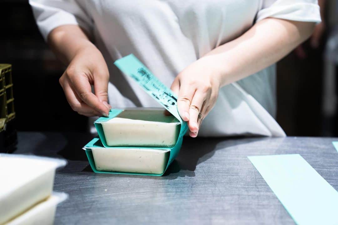 Ravo Bake Coffee Officialのインスタグラム：「手作業へのこだわり フィルムに印字してしまえば帯を巻く必要なんてなくなりますが、あえて時間と手間をかける事で愛着が湧いてくる その豆腐を求めて買いに来て下さるお客様に対しても沢山の愛を持って接する事ができる 7月も美味しい豆富を作って参ります  イートインメニューも夏メニュー試作中です お楽しみに」