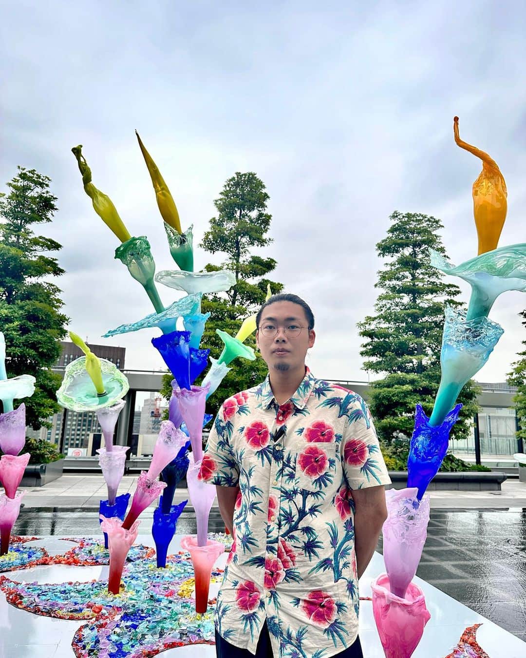 #ぶらエディターズ GINZA SIX オフィシャルさんのインスタグラム写真 - (#ぶらエディターズ GINZA SIX オフィシャルInstagram)「銀座とは思えないほど自然を身近に感じられ、訪れる人々に憩いの場を提供している屋上庭園、GINZA SIXガーデン🌿⛅️4〜5月には、グラフィックアーティストのYOSHIROTTENさん @yoshirottenによるアートパークが出現。パブリックなアートスペースとしても徐々に広がりを見せるこの場所に、ガラス素材を使った工芸作品や現代アートなど、ジャンルに囚われない作品を制作する若手ガラス作家、池上 創さん @chuangchishangによる作品が展示されています（📹1枚目）✨   池上さん（📸2枚目）は多摩美術大学工芸学科ガラスプログラムを卒業後、現在は“ガラスの街”と呼ばれる富山県富山市にあるガラス造形研究所に在学中。大学の卒業制作で手がけたインスタレーションをリメイクした『生命の息吹樹Ⅱ』が「ART AWARD　TOKYO MARUNOUCHI 2022」でグランプリを受賞し、その作品が大手アパレルメーカーのCMで使用されるなど、今注目されている若手ガラス作家なのです👏🏻✨   作品は、展示がスタートした環境月間である6月に合わせて、“サステナビリティ”をテーマとしたもの🌱🌎その名も「CIRCULATIONS」=循環。壊れても溶かして再利用できるガラスの特性に、枯れてもその葉が養分となり新しい命が生まれる植物になぞらえ、“再生”と“持続”を表現しています♻🍀   「直線的な建物が多い銀座の街が見渡せるこの空間に、あえてなさそうなものを作ろうと思いました。そこで植物からインスピレーションを得、カラフルで曲線的で、いい意味でこの場所に違和感が出る作品に仕上げました」。   カラフルなパーツは一つひとつ、口で吹いて膨らませて作られたといいます😳👏🏻「他の素材では行わない、“吹く”という行為がガラスの魅力のひとつだと思っています。たくさんの人々との出会いや、今までの人生を通して培われた経験などは全て自分を形成するエネルギーで、そのエネルギーを吹くことでガラスに注ぎ込み、膨らませることで具現化することができます。エネルギーが直接注ぎ込まれたパーツを組み合わせているので、綺麗なだけでなく、同時に力強さも感じてもらえると思います」。   小さなものでも3〜4人、大きなものになると総勢10名ほどのアシスタントの手助けのもと、息を吹いて制作したというガラスのパーツ。池上さんが“シワ”と呼んでいる先端の縮みの部分（📸3・4枚目）は、極限まで薄くなると熱に負けて縮んでいくガラスの性質を利用し、幾重にも繰り返して作っています（📹5枚目）。   「工芸の世界では吹いてグニャとシワになったら失敗とされますが、僕はそれが他の素材にはないガラスの面白さだと思い、そのシワを応用してこの技法を編み出しました。一回だと失敗に見えますが、重ねることでアートに昇華します」。   そうして約半年をかけて完成した「CIRCULATIONS」は、水が張られた水盤上に展示され、見る角度や昼（📸６枚目）、夕方（📸７枚目）、夜（📸８枚目）といった時間帯で印象が変わるのも見どころの一つ🙌🏻夜のライト演出は、池上さん自身も初の試みです✨また土台部分には、自身と他の学生の制作過程で出たガラスの破片が作品の一部として敷き詰められ（📸９枚目）、ガラスのサステナビリティとパワーを全体から感じられる作品となっています👏🏻   池上さんは最後に、「このGINZA SIXの展示のように、これからは日本ではあまり見かけないガラスのパブリックアートを展開していきたいと思っています。ガラスはパワフルで力強い素材。器などの工芸としてだけでなく、アートとしての魅力をもっと多くの人に伝えていきたいです。ぜひこの作品を見て、僕自身とガラスのエネルギーを感じていただけたらと思います」（📹10枚目）と今後の展望についても話してくださいました🌟   涼やかな水が流れる空間で、若手作家によるガラスのインスタレーションが見られるのは7/23（日）まで。時間帯によって見え方が変わる、様々な表情をお楽しみください✨   【池上創 Profile】 2000年神奈川県横浜市生まれ。2022年多摩美術大学工芸学科ガラスプログラム卒業。富山ガラス造形研究所在学中。　主な受賞歴に2021年「第一回宮若国際芸術トリエンナーレTRAiART」入賞、2022年「ART AWARD　TOKYO MARUNOUCHI 2022」グランプリ・オーディエンス賞がある。   #池上創 #soikegami #GINZASIXガーデン #屋上庭園 #展示#glass #ガラス #glassartist #ガラス作家 #art #アート #publicart #パブリックアート #sculpture #installation #インスタレーション #artist #アーティスト#contemporaryart #現代アート #contemporaryartist #アートのある暮らし #ginzasix_art #ginza #銀座 #ginzasix #ギンザシックス   @ginzasix_official」7月7日 12時12分 - ginzasix_official