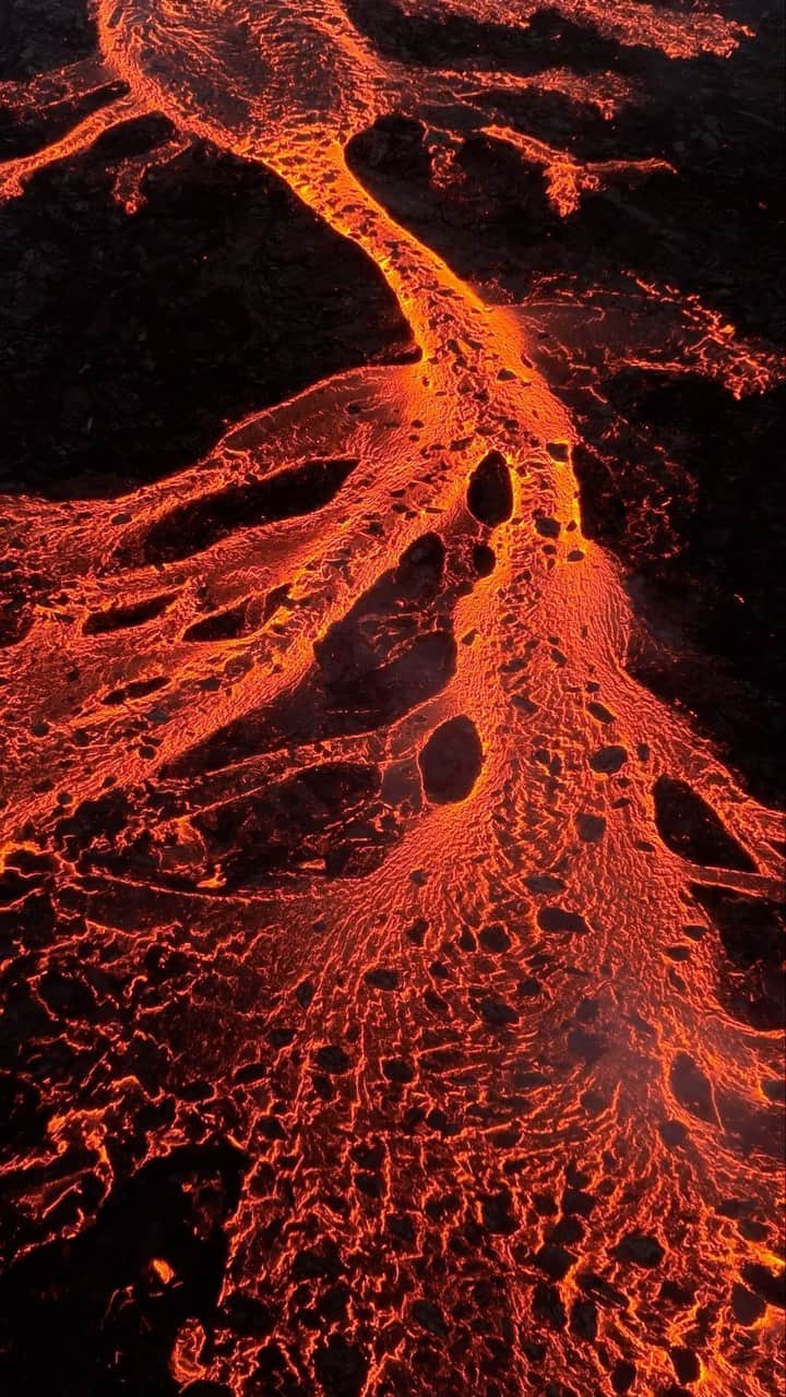 クリス・バーカードのインスタグラム：「As the latest volcanic eruption started, I was on the other side of the island having some quality family time, and decided that’s where I wanted to stay. Luckily my photo assistant @joelbarger_ who’s been busting his butt opening our gallery in Reykjavik was nearby. Sometimes I find it even more special to share in someone else’s witnessing something as powerful as this for the first time instead of documenting it myself. Grateful to be able to share his first views here  “After a series of frequent earthquakes heralding the arrival of another volcano on the Reykjanes Penninsula, I found myself crammed in the backseat of an SUV speeding towards the new eruption site to document it on behalf of @chrisburkard for @lavashowiceland & @rvkgrapevine  A 9km hike lay between us on the volcano due to the road closure, so we shouldered our bags and started jogging. Despite dense fog rolling over the hills, I crested the top and couldn’t miss the orange glow of the eruption visible about 2km away.  Every step closer felt like a entrance into a dream state, mesmerized by the dancing of magma shooting over 20meters in the air in some places.  Fortunately for me, a strong wind blew at my back keeping dangerous gasses away. Even so, ISAR warned us to vacate the area soon after shooting some photos with the expectation that winds could shift and the gas could prove hazardous, even deadly to visitors.  The fissure is over 1km long, 10-15 times the size of the previous year’s eruptions and shook the ground at our feet in a powerful rumble… serving as a reminder of the sheer magnitude of new earth surfacing from below.  Around 1:30AM, the police arrived and started directing everyone to leave, conditions deteriorating. I could have stayed for hours, feeling absolutely no sense of time and fatigue, just literal awe and exhilaration at the foot of an active volcano.”」