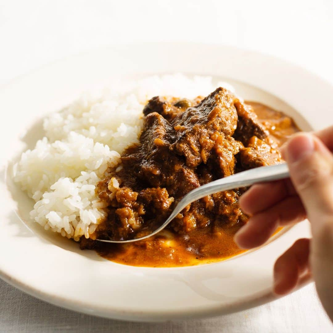 BALMUDA (バルミューダ) のインスタグラム：「夏に食べたい、こだわりカレー。水野仁輔のビーフカレー . 炒めてから、ひたすら煮込む。スパイスについての料理教室や多くの著書を手掛けるカレー研究家 水野さんが教えてくれた本格カレーのレシピを紹介します。スパイスが効いた味わい豊かなカレーと、BALMUDA The Gohanの粒立ちの良いごはんの相性は抜群！クセになること間違いなしです。スパイスを揃えれば手順はとてもシンプル。この夏は、こだわりの家カレーをご堪能ください。 . 水野仁輔のビーフカレーのレシピ . 【材料】 植物油...大さじ3 しょうが（すりおろし）...1片 トマトピューレ...大さじ4 塩・こしょう...小さじ1 牛肉（肩ロース、モモ、バラなど）...500g プレーンヨーグルト...100g 水（できればチキンブイヨン）...400ml はちみつ...小さじ1 バター（あれば）...20g . ＜ホールスパイス＞ カルダモン...6粒 ビッグカルダモン...1粒 クローブ...5粒 シナモン...1本 玉ねぎ（みじん切り）...大1個（300g） にんにく（すりおろし）...1片  ＜パウダースパイス＞ ターメリック...小さじ1/2 ホワイトペッパー...小さじ1/2 レッド・チリ...小さじ1 ガラムマサラ...小さじ1強 クミン...小さじ2 コリアンダー...小さじ2 . *レッド・チリをパプリカパウダーに代えると子どもや辛いのが苦手な方も食べられます。 * パウダースパイスを各種揃えられないときは、カレー粉でも可。 . 【作り方】 １．鍋に植物油を入れて中火で熱し、ホールスパイスを加えて炒める。カルダモンがふくれてくるまで。香りを引き出したい場合は、油が冷たいうちに加える。 ２．玉ねぎを加えて塩少々(分量外)を振り、強火で濃いきつね色になるまで炒める（目安時間：約15分）。強火のままにんにく、しょうがを加えて、水分が飛び、青臭い香りがなくなるまで炒める。途中、小さじ2〜3ほどの水（分量外）を何度かに分けて加えながら炒めると時間を短縮できる。 ３．トマトピューレを加えて水分がほぼ飛ぶまで炒める。 ４．弱火にし、パウダースパイスと塩を加えて炒める。スパイスにしっかり火を通したいので、1分以上は炒めたい。少量の水を加えて2〜3分炒めると香りはより立ちやすい。 ５．牛肉はひと口大に切って、塩、こしょう（分量外）を多めに振る。鍋に加え、中火にして表面全体が色づくまで炒める。ここでカレーのベースと牛肉とをよくなじませる。 ６．中火にし、よく溶いたプレーンヨーグルトを加えてざっと混ぜ合わせる。水を2回に分けて注いで強火でその都度煮立てる。水の代わりにチキンブイヨンを使うとよりうま味が増す。弱火にしてはちみつを加え、ふたをして60分ほど(できれば90分ほど)煮込む。火はできるかぎり弱火にする。それでもふたをして煮込むと鍋中は表面がぷくぷくとするくらいの温度まで上がる。 ７．煮込みが完了したらふたを空け、バターを溶かし混ぜ、必要なら塩で味を調整する。 . . #BALMUDA #バルミューダ #カレー #水野仁輔 #本格カレーレシピ #スパイスカレー #スパイスレシピ #素晴らしい夏を」