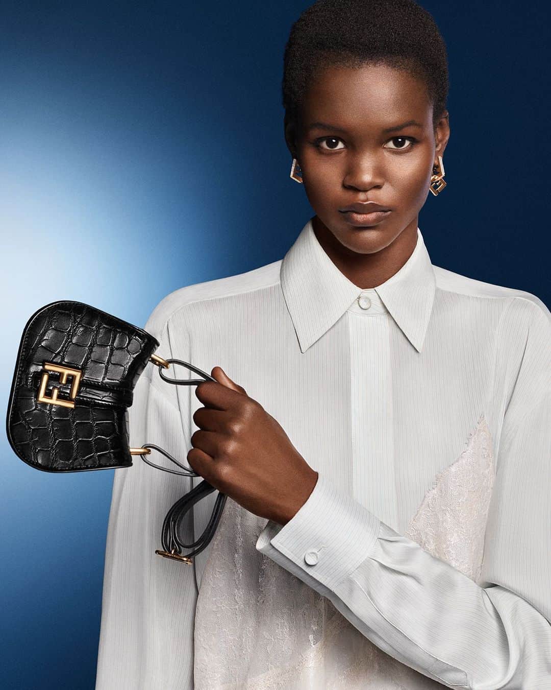 Fendiのインスタグラム：「Apparently simple, yet requiring complex craftsmanship. The #FendiFW23 campaign expresses a concept at the heart of the Maison through a precious iteration of the new #FendiCmon satchel and a dress with trompe l'oeil lace detailing.  Artistic Director of Couture and Womenswear: @mrkimjones​ Artistic Director of Accessories and Menswear: @silviaventurinifendi ​ Artistic Director of Jewellery: @delfinadelettrez​  Creative Direction: @ronnie.cooke.newhouse @karlbolander  Photography: @craigmcdeanstudio  Styling: @themelanieward Hair: @anthonyturnerhair Makeup: @peterphilipsmakeup  Casting: @shelleydurkancasting Set Design: @alexanderbockstudio  Model: @migoaguol」