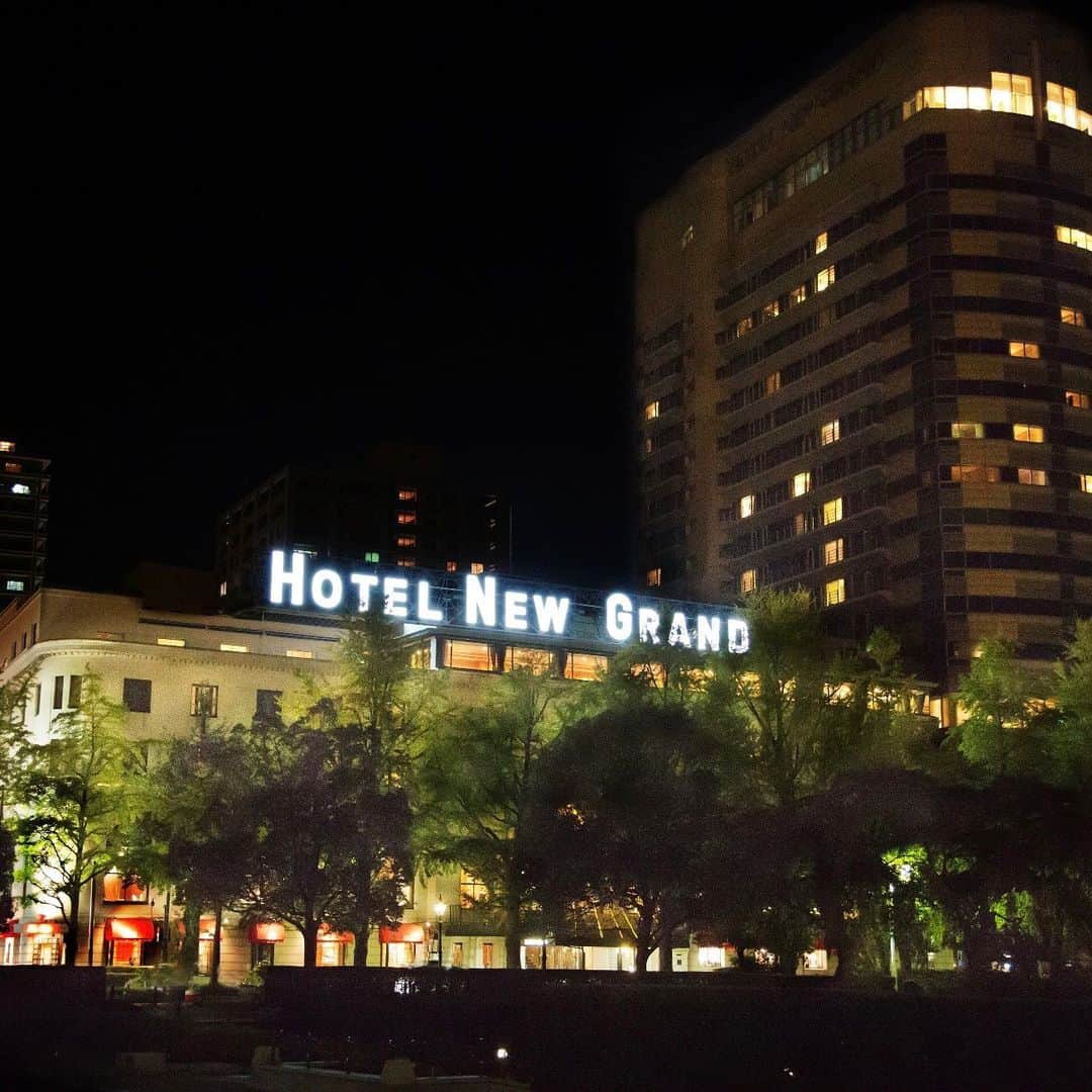 【公式】ホテルニューグランドのインスタグラム：「＊ 7/15はネオンサインの日。 本日は本館屋上に灯るネオンを紹介いたします。   ホテルの屋上にネオンの明かりが初めて灯ったのは1964年の東京五輪の時。しかし、第一次オイルショックが起きた1973年に省エネのため消灯しネオン管は取り外され、文字の枠組みのみ残されていましたが、2020年の東京五輪を見据えた改修工事を期に「横浜の象徴ともいえるネオンサインをお客様にも楽しんでいただきたい」という想いから再点灯を決め、2014年にネオン管が復活しました。 再点灯に際しては、LEDを使用することも検討しましたが、やわらかくて温かみのあるネオン管を採用しました。    行きかう船や人々を見守り、 いくつもの年月を過ごしてきた HOTEL NEW GRANDのネオン管。  ホテルへご来館いただいた際はもちろん、 横浜へお越しの際にはぜひ ネオン管に込められた様々な想いを 感じていただけたら幸いです☺️✨   #ホテルニューグランド #横浜 #クラシックホテル #横浜ホテル #ネオン #ネオン管 #ネオンサイン #灯り #夜景 #光 #イルミネーション #歴史 #外観 #建築物 #建築デザイン #オリンピック #シンボル #山下公園 #hotelnewgrand #yokohama #neon #neonsign #nightview #classicstyle」