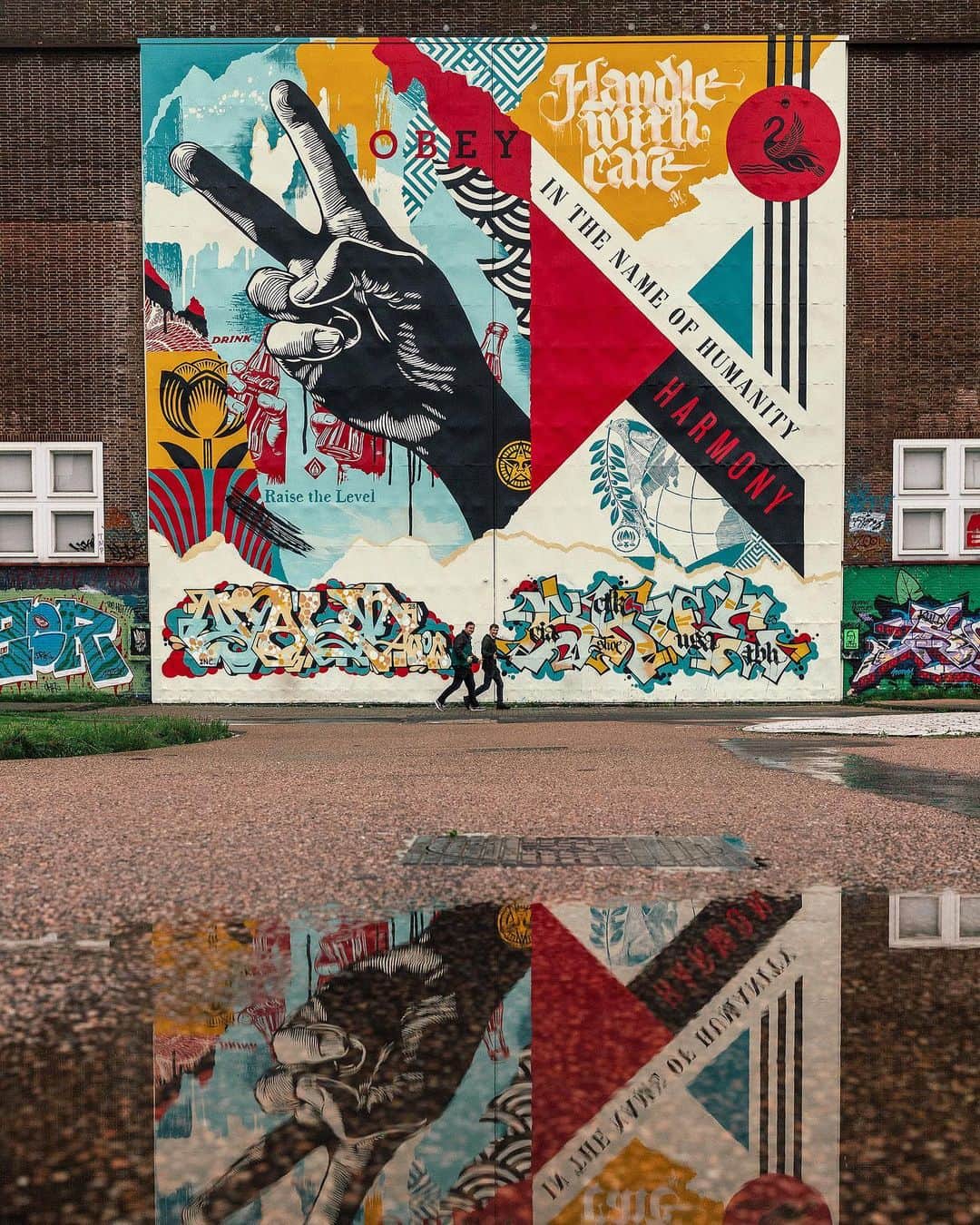 Shepard Faireyのインスタグラム：「Reflecting on my mural at the Straat Museum in Amsterdam, I feel very lucky that though it rains a lot here, the weather allowed us to finish the mural on time despite some intense winds. The Straat is a huge old factory where they built ships so the surface I painted is a set of metal doors 45 feet high formerly used to get the ship parts out of the building. The doors are a smooth surface and provided an ideal canvas for the “Raise the Level” mural. The mural is based on one of my art pieces focused on peace and harmony which is included in my exhibition at Straat. I also added some additional text and imagery to fit the composition of the doors. I have been friends with Amsterdam local and calligraffiti pioneer Niels Shoe Meulman for over 10 years and I asked him if he would collaborate on part of the mural. He generously added the “Handle with Care” in his unique style as well as a wild style piece down below. He also brought his friend, and O.G. graff writer Yalt to do the piece on the lower left. I’m very happy about the street art and graffiti hybrid of the entire piece because I believe the two genres are driven by the same spirit. Also, the Straat Museum celebrates and showcases both movements. I’m very grateful to my crew of Dan Flores, Rob Zagula, and Jon Furlong for their hard work helping with the mural. Thanks to @jonathanfurlong also for the great photos. A huge thanks to the Straat crew for hosting and being incredibly pro about EVERYTHING. Check out my show “Raise the Level” at Straat if you are in Amsterdam! -Shepard」