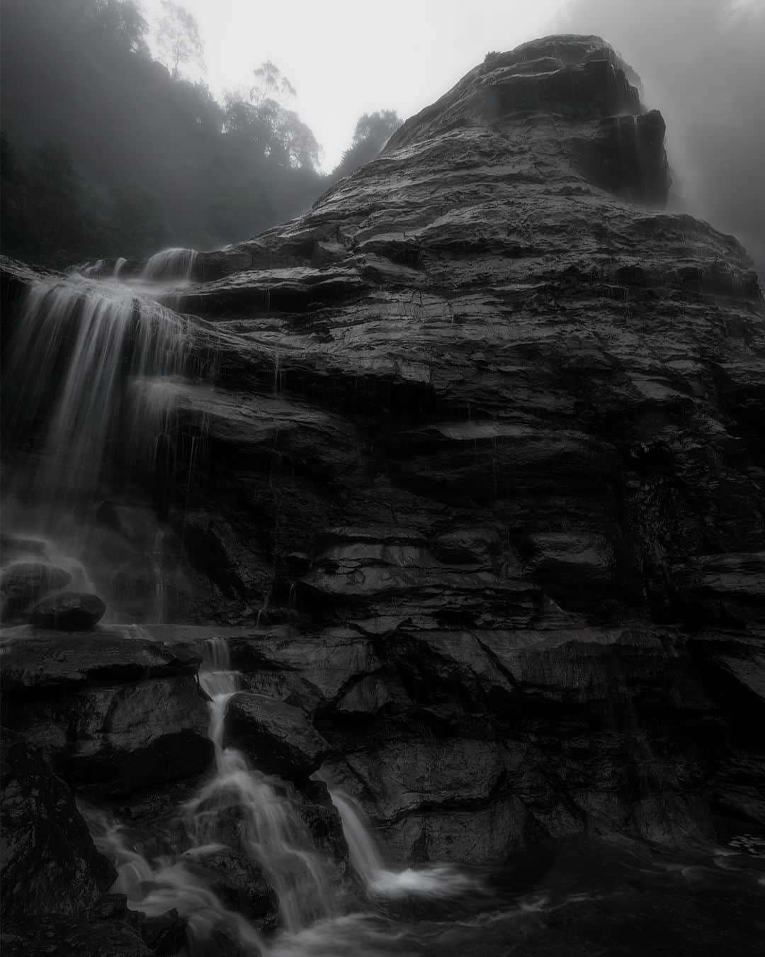 Nikon Australiaのインスタグラム：「Embracing the harsh conditions of rain and fog can produce ethereal results and this was certainly the case for @ivanzafiris_ in his trip to the Blue Mountains with the Z 7II.   "On a recent trip to the beautiful Blue Mountains in Katoomba, the opportunity presented itself with all the recent rain to get out and shoot some waterfalls.  Most of the tracks were closed due to quite significant landslides that had occurred with a lot of trees and logs making their way down the waterfalls, and as such some of the popular waterfall's tracks were closed. For this shot even though there had been enough rain, there wasn't much water flowing down Bridal Veil Falls but luckily, we had significant fog that hovered around and on top of the waterfall.   This took me a while to shoot as I couldn't quite get the right composition I was looking for, as I wanted to include some of the water flowing towards the left of the waterfall down the rock and also include that huge rock structure and fog, that was sitting on top of the waterfall. After a good 30 minutes, I managed to walk away with a final shot that I was happy with, and for this shot I wanted it to be black and white to bring out the drama with the fog, the black rocks, and the water trickling down the side of the waterfall."  Photo by @ivanzafiris_  f/11 | 1/4 sec | ISO 64  Captured on the Z 7II and NIKKOR Z 14-24mm f/2.8 S  #Nikon #NikonAustralia #MyNikonLife #NIKKOR #NikonZ7II #Z7II #LandscapePhotography #WaterfallPhotography #BlueMountains #Australia」