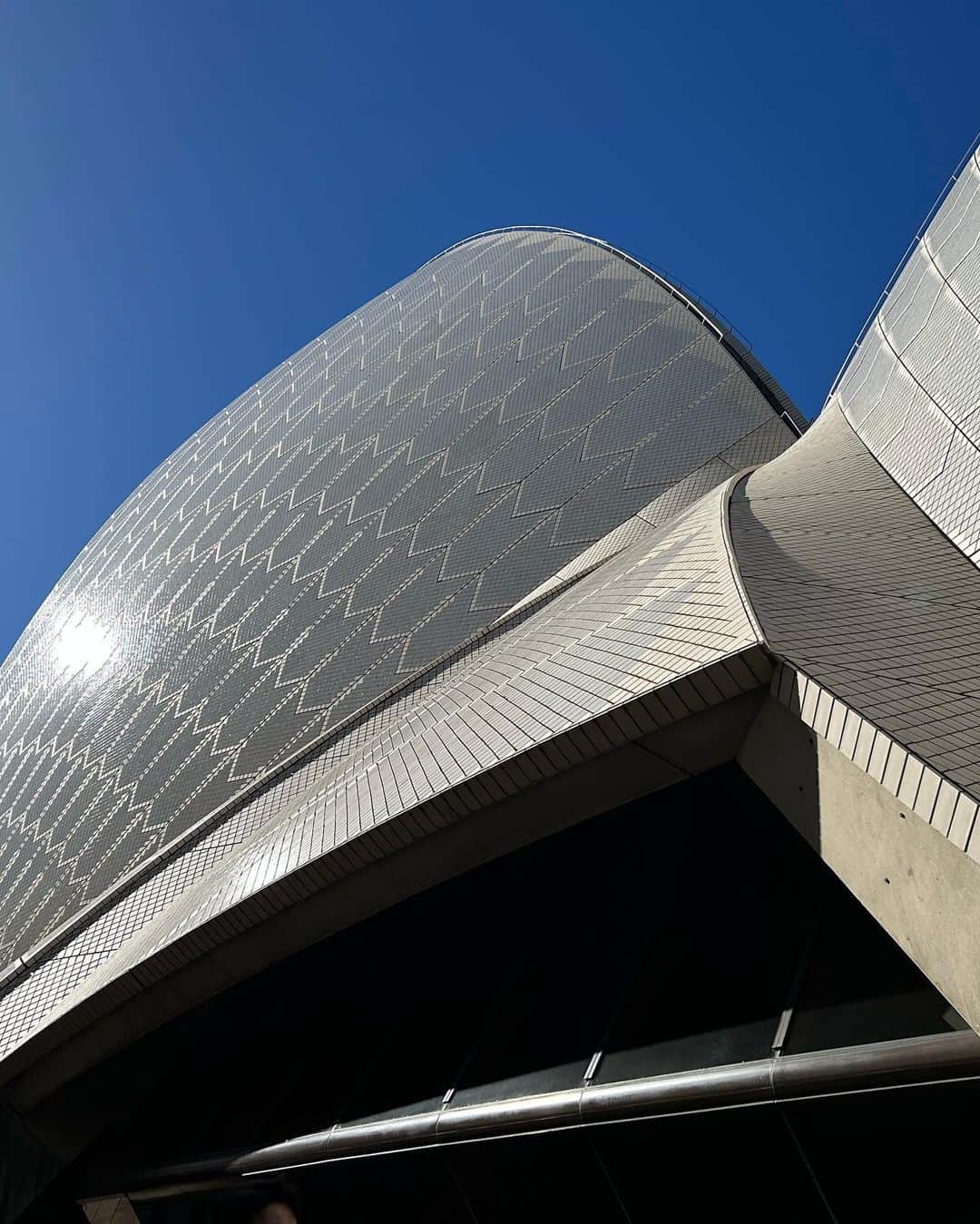 中岡由佳さんのインスタグラム写真 - (中岡由佳Instagram)「❇︎ 12時からのオペラハウス館内見学ツアー、ガイドはTakakoさん。天井がないエレベーターを初めて見て驚き。オペラハウスの歴史を聞き今ここに建つまでの年月の重さを知りました。1956年オペラハウス建築のために実施された国際デザインコンペで選ばれたデンマーク人若手建築家ヨーン・ウッツォン。斬新的で独創的なオペラハウスはそのデザインの複雑さで工事は難航。もともと3〜4年の工期を予定でしたが建設費用を予算を大幅に超え、工事は遅れ、新政権と折り合いがつかなくなったウッツォンは辞職に追い込まれデンマークへ帰国。外観はウッツォンの建築デザイン、内観はオーストラリアの建築家チームが引き継ぎ、1956年の着工から14年経た1973年に完成しました。エリザベス女王臨席のもと落成式が行われましたが、ウッツォンは招待を辞退し、建築離脱後はオーストラリアを一度も訪れてはいないそうです。2007年にオペラハウスは世界文化遺産に登録。「人類の創造的才能を表す傑作である」というひとつの基準で登録が認められました。ウッツォンが亡くなる前年に世界文化遺産に登録されたので、その吉報を耳にする事が出来た事は、ウッツォンがオペラハウスデザインを手がけた建築家人生においてせめてもの救いだと思いました。 オペラハウスのヨットの帆orシェルのような曲線の屋根にはスウェーデン製のタイルが105万6000枚使われていて、光沢のある白いタイルとクリーム色の2種類が組み合わされています。白いタイルだけがキラキラっと光り、光が波打つようにデザインされています✨タイルは汚れがつきにくい特殊な加工がされていて、雨がタイルを綺麗にしてくれるそうです🌧️まだパソコンもない時代、ウッツォンがデザインしたシドニーオペラハウスの素晴らしさに感動しました🥹 @sydneyoperahouse  #sydneyoperahouse  #JornUtzon #sydney #australia  #winter」8月1日 4時37分 - yuka_nakaoka