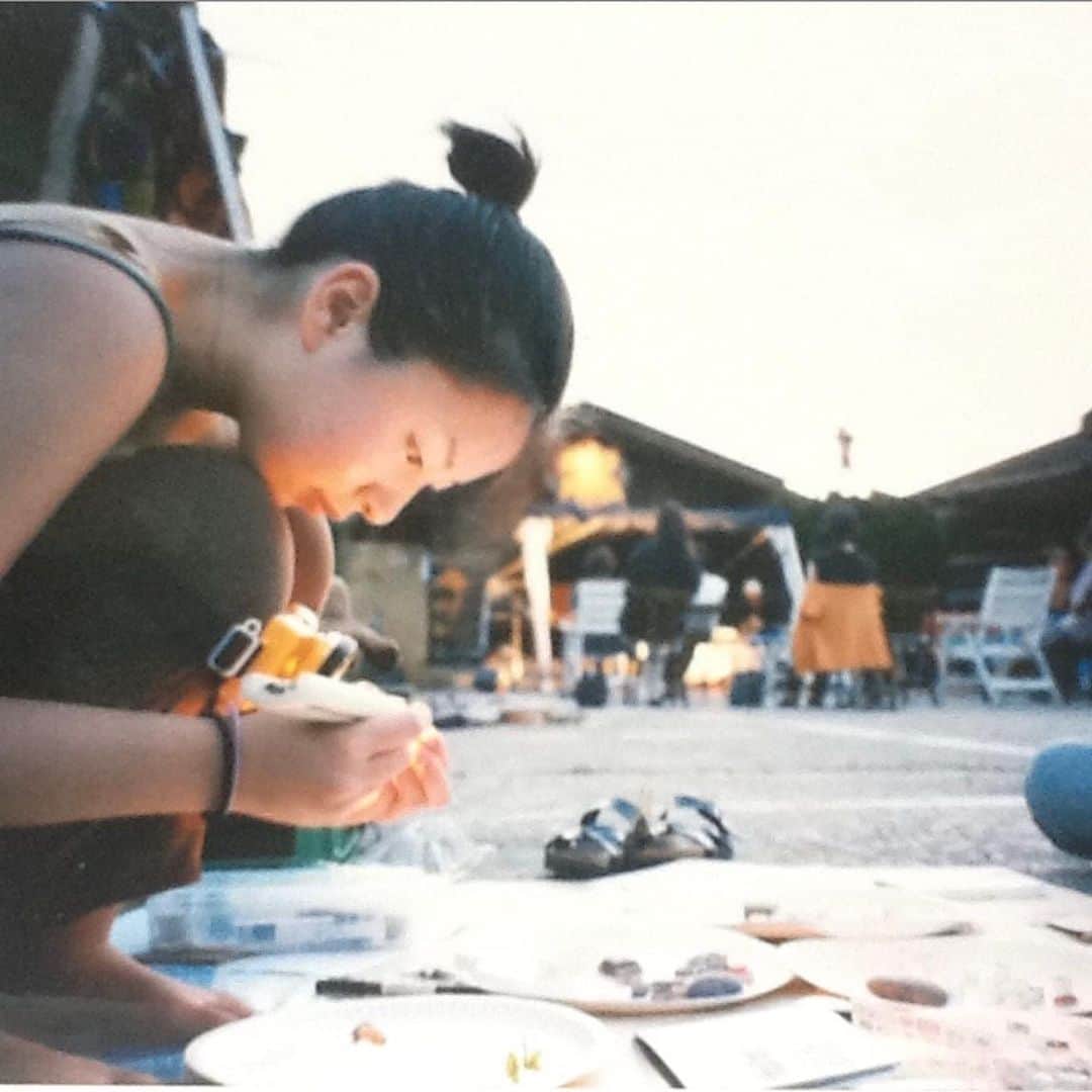 津久井智子のインスタグラム：「これ☝️ 20年前の今日、 「はんこや象夏堂」がこの世にデビューした日の写真です😆  2003年8月1日 千葉県市原市の山にあった 多国籍レストラン 「キッチン🌀アルボル」 の駐車場で催された3日間の夏祭り 「まったりフィエスタ」にて 初めて「象夏堂(ショウカドウ)」と屋号をつけて、自作のはんこに値段をつけて、販売してみた日。  炎天下にゴザ敷いて、いろんな人の弾き語りライブを聴きながら、お客さんにリクエストされた絵柄で下絵を描き、瓶にライム刺さったコロナビール片手に、ススムさん達の焼く美味しいタコスをかじりながら、はんこを一心不乱に彫り、面白い魅力的な大人たちに出会い、オーダーメイドの楽しさにのめり込み、気づいたら両耳の後ろが日焼けして真っ赤に腫れ上がり、水膨れができていたくらいに、夢中になっていました。  自分の「これかも！」という道を見つけたような気がした日。  お祭りも夏の山も、音楽もタコスも、集まった人たちが皆楽しそうに笑っているのも全てが最高で、「こんなお祭りみたいな中で、好きな人達と楽しみながら自分の得意なことで仕事して生きられたら幸せだなぁ」と、笑っちゃうくらい甘いけど本気で願えば叶わなくもない夢を真剣に描いたのでした。  そうして走り走るうちに、縁が縁を呼び、奇跡のようにたくさんの巡り合わせや力をいただいて、こうしてひとつの稼業としてどうにか20年間成り立つことができました。  この20年の間に関わってくれた、全ての方に感謝しています🙏  願わくば、見た人の心が少しでも軽く明るくなったり、ワクワクするような作品をたくさん作りたい。届けたい！  そのためにはまず、自分の心と体が健やかで幸せで満たされていることが大事だということも、少しずつ学んできています。  この先もどんどん軽やかに、旅するように、楽しく制作を続けたい！ 気持ちを新たに、深呼吸しています。 これからも応援よろしくお願いします😊」