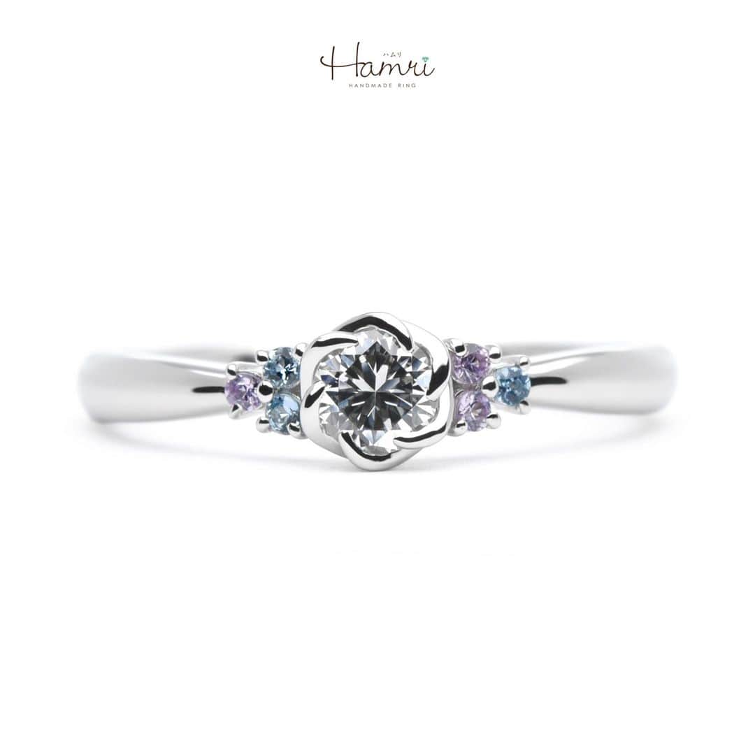 結婚指輪・婚約指輪『Hamri(ハムリ)』のインスタグラム：「【手作り婚約指輪】  お相手様のことを想いながら、細部までこだわってくださった ダブルサイドメレの婚約指輪です。  センターダイヤモンドはお花の石枠で可憐な印象に。  サイドに留まったバイオレットサファイアのパープルと アクアマリンのブルーが、上品な可愛らしさをプラスしてくれています。   内側にはお二人の記念日とお名前が刻印されており 他にはない素敵な婚約指輪となりました！  ご婚約おめでとうございます！  ==========================  ♦︎♢指輪制作の写真や動画を無料撮影、全データプレゼント♢♦︎  DMやLINEでのご相談お待ちしております♥ ⇒@hamri_omotesando  ❁・❁・❁・❁・❁・❁・❁・❁・❁・❁・❁  ＊結婚指輪・婚約指輪セットリング5%OFF＊  @hamri_omotesando  Hamri「ハムリ」  〒150-0001 東京都渋谷区神宮前5-11-11 2F  tel 0120-121-175 hp https://hamri.jp/  open 11:00〜19:00 close 火/水　祝日営業  ❁・❁・❁・❁・❁・❁・❁・❁・❁・❁・❁  #手作り結婚指輪 #手作り婚約指輪 #婚約指輪 #マリッジリング #エンゲージリング #プレ花嫁 #Hamri #Hamri表参道 #オーダーメイドリング #鋳造 #ブライダルリング #ペアリング #サファイア #プラチナリング #アクアマリン  #婚約指輪探し  #2023wedding #2023春婚 #2023夏婚 #プレ花嫁準備 #プレ花嫁と繋がりたい #結婚指輪探し #結婚指輪選び #結婚準備  《Hamri検索タグ》  #Hamriデザイン #Hamri指輪作り #Hamri花嫁」
