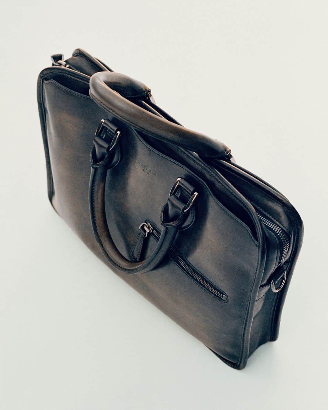 ベルルッティのインスタグラム：「- DISCOVER THE ICON: UN JOUR BY #BERLUTI -   The devil is in the details: hand-cut and sewn, the finishing touches of the Un Jour briefcase include delicately rounded leather strips, palladium-finished metallic details, a trolley loop and a distinctive zipped front pocket.   Now available online and in-store.   Photography by @deo_suveera   #ICONSBERLUTI #BERLUTISAVOIRFAIRE」