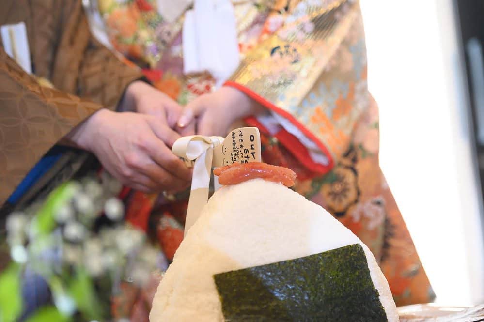 のインスタグラム：「【おにぎり入刀🍙おにぎりバイト】  ウェディングケーキに入刀はこれまで見たことがある方もいらっしゃるかも知れませんが、今回はなんとおにぎり入刀&バイト！！！  お二人の大好きなおかず、明太子を上にちょこんと乗せて、手づくりしゃもじで入刀☺️  そしてまだまだここから！ 両家のお母様におにぎりを手作りしていただき、新郎新婦様へ愛情を込めたおにぎりバイト🍙  そこから次は新郎新婦様から、お母様達へ愛情伝わっているよ、いつもありがとう！の想いを込めたおにぎりを握ってサンクスバイトでお返ししました🍙🍙  誰とも被らないお二人ならではのセレモニー！ 何でもお手伝いさせていただきます！皆様はどんなセレモニーがしたいですか？😌 －－－－－－－－－－－－－－－－－－ ⁡フェアのご予約・卒花レポートは  ▷ 会場見学・フェアの予約 ▷ スタッフブログ ▷ 結婚式レポート ▷ 特典・料金プラン ▷クチコミ情報 は ︎︎  【@aquadebutsaga】のTOPページ 【lit.link/aquadebutsaga】を要チェック︎︎︎︎✔ ⁡ －－－－－－－－－－－－－－－－－－ ⁡ #アクアデヴュー佐賀スィートテラス#ナチュラルウエディング#ガーデンウェディング#佐賀結婚式#佐賀結婚式場#福岡結婚式#式場レポ#式場見学#結婚式レポ#挙式レポ#佐賀花嫁#日本中のプレ花嫁さんと繋がりたい#ブライダル#ブライダルフェア#コロナ禍の結婚式#結婚式準備#くふう婚#卒花#プレ花嫁オリジナルウェディング#カラードレス#ウェディングドレス#バイト#ファーストバイト#おにぎり#おにぎり入刀」