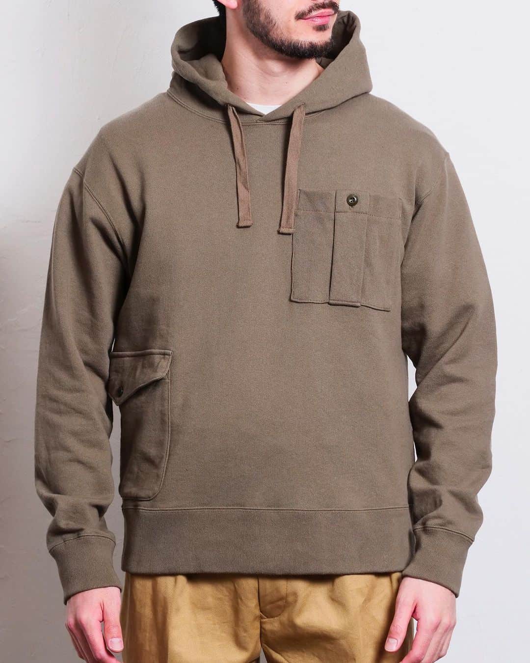 サウンドマンのインスタグラム：「Soundman '23AW Collection item "Clayton"(クレイトン)  ブリティシュアーミーのカーゴパンツに見られる特徴的なアシンメトリーに配されたポケットディティールを裏毛フーディーのボディに載せたユニークかつ使い勝手の良い１着。  素材はリサイクルコットンの空紡糸で編み立てた裏毛。  ドライタッチでデッドストックに水を通したような風合いをイメージ。  *Hoodie with British army Cargo pants Pockets  *Fleece knitted with recycled cotton  *urea button  *Boxy fit  *Flat cord with hood  *Product washed   #soundman #サウンドマン #2023aw #heritagestyle #vintagestyle  #heritagemenswear  #横浜 #山下公園 #yokohama #military  #hoodie」