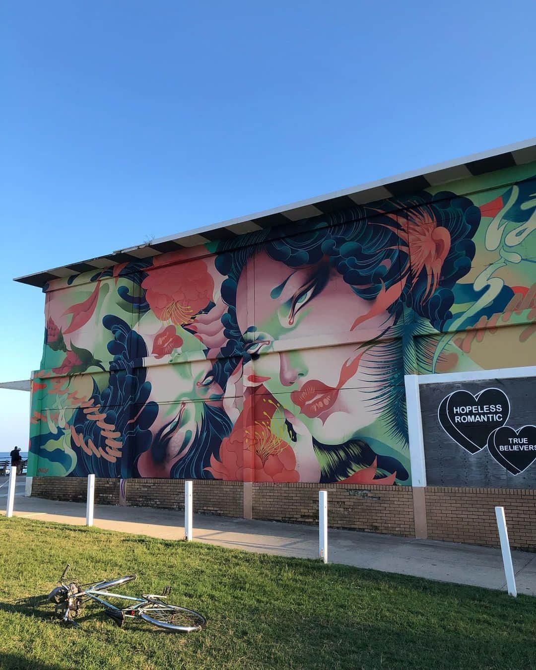 岡田育のインスタグラム：「Here’s the extravagant main dish of my short trip!! The latest huge mural by ONEQ for the Wooden Walls Project. @woodenwallsproject  #woodenwallsproject #asburyparknj  #oneq #harahara #asburyparkboardwalk   The title “HARA HARA (はらはら)” has two meanings in Japanese; the sound of falling petals that show the impermanence of our world, and the hidden heart races in our wish. Cross-cultural conversations are always thrilling and have some tensions, but hope we’ll get more fruits from it 🪷☎️🤙 See also @negiyakisoba for the artist's statement. #noplaceforhate  . ONEQ, the Japanese artist had residented in Asbury Park for weeks and done THIS all by one’s hand with no assistants but the big red skyjack lift. I could finally visit one of the mural works of my friend and talk a lot about love, peace, and joy around the  #publicarts worldwide network. Congratulations ONEQ!!  ⚡️⚡️👏🥳👏⚡️⚡️ . 小旅行の目玉！！ 我が友ONEQさんの最新作「HARA HARA」完成ほやほやを拝んでまいりました！！ サイズちゃんと伝わりますかね、圧巻よ！！ この規模を一人で描くアーティストはそう居ないそうで、道行く人々みな驚いていた。数週間の滞在ですっかり街に馴染んだご様子、今後も描きにくる予定があるそうです。」