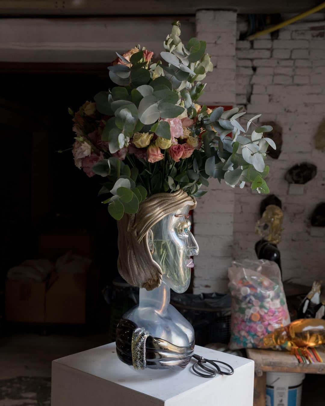 New York Times Fashionのインスタグラム：「Is this what Anne Hathaway, Jackie Kennedy and Jean-Michel Basquiat would look like if they were rendered out of glass?  The artist Hugh Findletar creates bust-like vases out of glass — interpretations of both famous and non-famous faces — which he calls “flowerheadz.” He has made versions inspired by people such as the model Naomi Campbell, a doorwoman who works at his apartment building in Milan and Solomon, the biblical king.  In September, @mr.flowerheadz will introduce new vases at Bergdorf Goodman in Midtown Manhattan, as part of a group art show hosted by the Spaceless Gallery in the department store’s home décor section. Some of the pieces that will be there are modeled after people connected to New York, including the jazz singer Billie Holiday; Patricia Field, the merchant turned “Sex and the City” costume designer; and Jacqueline Kennedy Onassis.  Findletar works out of glassblowing workshops on Murano, the Italian island near Venice known for its centuries-old glass industry. He typically works with five other artisans to create each flowerheadz vase. (Ears are applied last.)  He is among a handful of Black glass artists who have penetrated the glassmaking industry in Venice, said Adrienne Childs, an art historian and an associate at the W.E.B. Du Bois Research Institute at Harvard. In an interview with The New York Times, Findletar said he sees making the flowerheadz vases as a way of trying to repopulate the planet with “my people of every color, even green.”  Tap the link in our bio to see more of Findletar’s distinctive glass vases. Photos by @demayda」