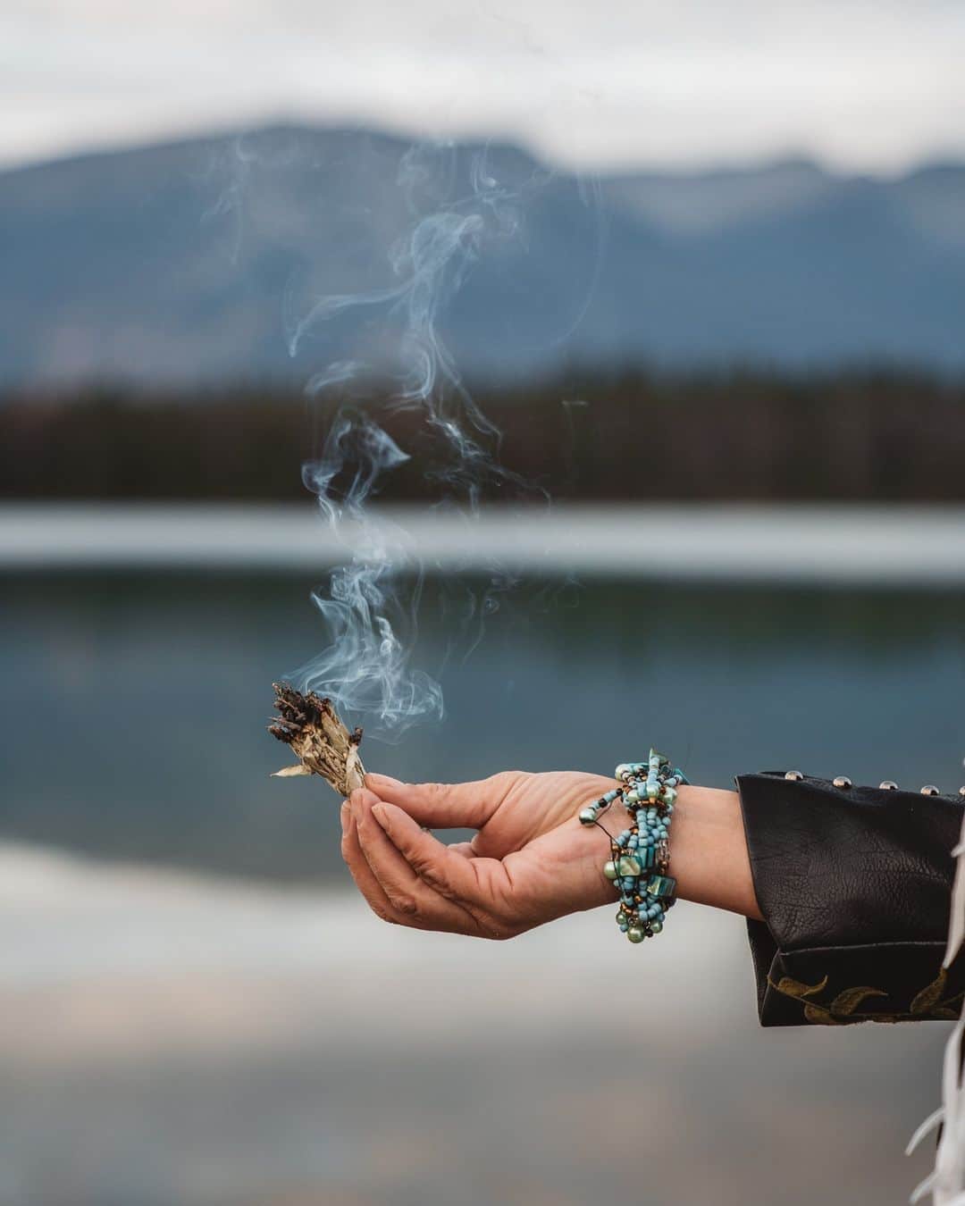 Explore Canadaのインスタグラム：「Important words from our friends at @destinationindigenous:   “The future is Indigenous 🪶:  In a world struggling with the results of global warming and pollution, the key to the future may be found in ancient knowledge of the past. The Indigenous Peoples of Canada have a special relationship with the earth and all things in it. According to Indigenous beliefs, plants, animals, water, and other resources are gifts of Mother Earth that should be treated with great respect. As stated at the United Nations Framework Convention on Climate Change in 2015, “Indigenous peoples have known for thousands of years how to care for our planet. The rest of us have a lot to learn and no time to waste.” Traditionally, Indigenous hunters, gatherers and fishermen took only what they needed, used all that they took, and gave thanks for the bounty. They consider themselves not to be owners of the land, but stewards with the responsibility to preserve the land and its resources for future generations. This age-old knowledge of the land could be the key to a brighter future for everyone. As Indigenous leaders work to help, inspire, and empower the next generation, they are building a better future where all people - including Indigenous nations can share and celebrate who they are.”  #DestinationIndigenous | #ExploreCanada | #TheOriginalOriginal  Image description: A close up of a hand holding a small handful of burning sage. In the blurred background is a large body of water with mountains looming over.」