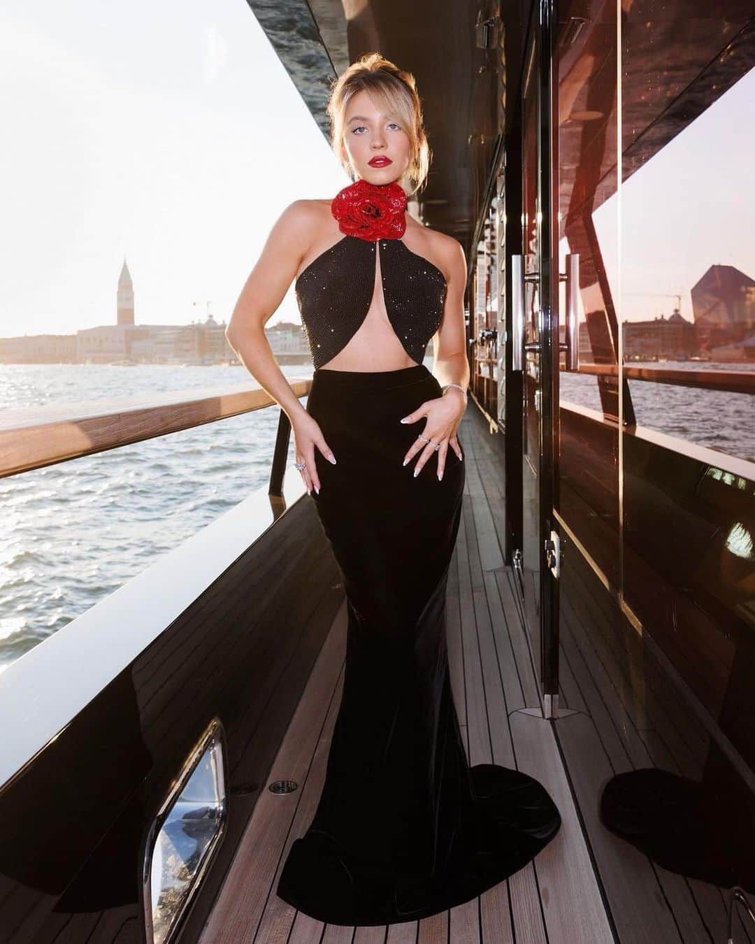 Harper's BAZAARのインスタグラム：「@sydney_sweeney made a gorgeous appearance at the Armani Beauty dinner during the Venice International Film Festival, where she wore a slinky halter gown featuring an ab-baring cutout torso, a small circular train, and a lacquered rose at the neck. She accessorized the piece with dainty diamond jewelry and added a matching red lip. Tap the link in bio to see all the looks from the star-studded festival so far.  Photo: @nailsbyzola via Instagram」