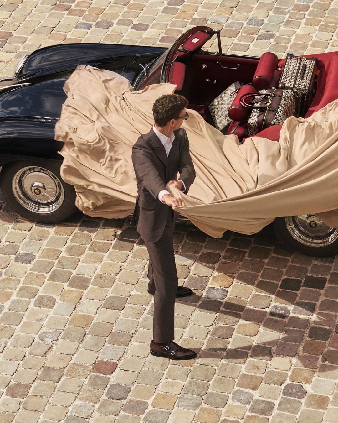 ベルルッティのインスタグラム：「- TRAVEL ICONIC: TOILE MARBEUF BY #BERLUTI -   An effortlessly chic suit. A vintage car with an eccentric twist. A dramatic luggage set: the Berluti man hits the road away from the city skyline and towards the glowing vineyards.   The reveal: A new season means an invitation to discover a fresh way of traveling, where a modern, relaxed mood meets a hint of nostalgia, embodied in the Toile Marbeuf line, a new design that pays homage to the heritage of the house, the Berluti way.   Now available online and in-store.   Creative direction by @trendsandculture for Berluti  Styling by @benmartinengo  Video by @danielrieraofficial Model: @thibaudcharon   #BERLUTITOILEMARBEUF」