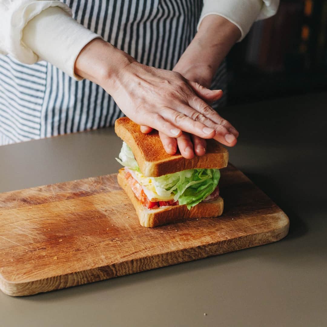 北欧、暮らしの道具店さんのインスタグラム写真 - (北欧、暮らしの道具店Instagram)「おいしさの秘密は重ねる順番。 とろっと卵とチーズが嬉しい「定番サンドイッチ」 . - - - - - - - - - - - - - - - - - 思わずごきげんになってしまう サンドイッチレシピを教えてくださるのは、 料理家の小堀紀代美（こぼり きよみ）さんです。  家にある材料ですぐできる、 定番のサンドイッチをご紹介します。 . - - - - - - - - - - - - - - - - - いちばんシンプル、いちばんおいしい。 小堀さん家の定番朝サンド - - - - - - - - - - - - - - - - -  【材料（2つ分）】 食パン…2枚（6枚切り） レタス…2〜3枚 ハム…1枚 チーズ…1枚 トマト…2枚（1cmほどの輪切りで） 卵…1個 バター…10g マヨネーズ…大さじ1  ※今回のレシピではももハムとゴーダチーズを 使用していますが、スライスチーズなど お好みの種類でOKです  【下準備】 レタスはほんの少しの塩（分量外）をふって 食パンの大きさよりやや小さめに 折りたたんでおく。  【作り方】 ❶食パンはトーストして、 両面の内側にマヨネーズをぬる。  ❷スクランブルエッグを作る。 卵をボウルに溶きほぐし、 塩少々（分量外）を入れてよく混ぜる。 フライパンにバターを入れて 強めの中火にかけ、バターが溶けたら 卵液を入れる。 ゴムベラで大きくまとめて 半熟のうちに取り出す。  ❸パン、トマト、ハム、チーズ、 スクランブルエッグ、レタス、パンの順に 重ねたら、上からぎゅっと押して馴染ませる。  ❹大きめにカットしたクッキングシートの 中央にサンドイッチを置く。 シートの上下の端をあわせて、 1cm幅で折りたたんでいく。 左右の端は上から押さえながら三角形に折り、 底面のほうに折り曲げる。 半分にカットしたら完成。 . - - - - - - - - - - - - - - - - - ■ 小堀さん  「サンドイッチをべちゃっとさせずに おいしく作るコツは、 パンの内側にバターやマヨネーズなどの油脂を しっかり塗ること。  それから、重ねる順番も大切です。 今回だと、チーズの上に 温かいスクランブルエッグをのせることで とろっとした食感が楽しめます。 ハムやチーズの塩気でレタスを食べたいときは、 それらを隣どうしにするのもいいです。  色々試して、おいしい重ね方を 見つけてみてくださいね」 . - - - - - - - - - - - - - - - - - . #kitchen#kitchendesign#kitchenware#food#foodstagram #サンドイッチ#レシピ#サンドイッチレシピ#お弁当#ランチ#お昼ご飯#夜ご飯#今日のごはん#小堀紀代美 さん#家じかん#料理#キッチン#キッチン雑貨#シンプル#シンプルライフ#シンプルデザイン#暮らしを楽しむ#日々の暮らし#北欧#暮らし#北欧暮らしの道具店」9月4日 17時01分 - hokuoh_kurashi