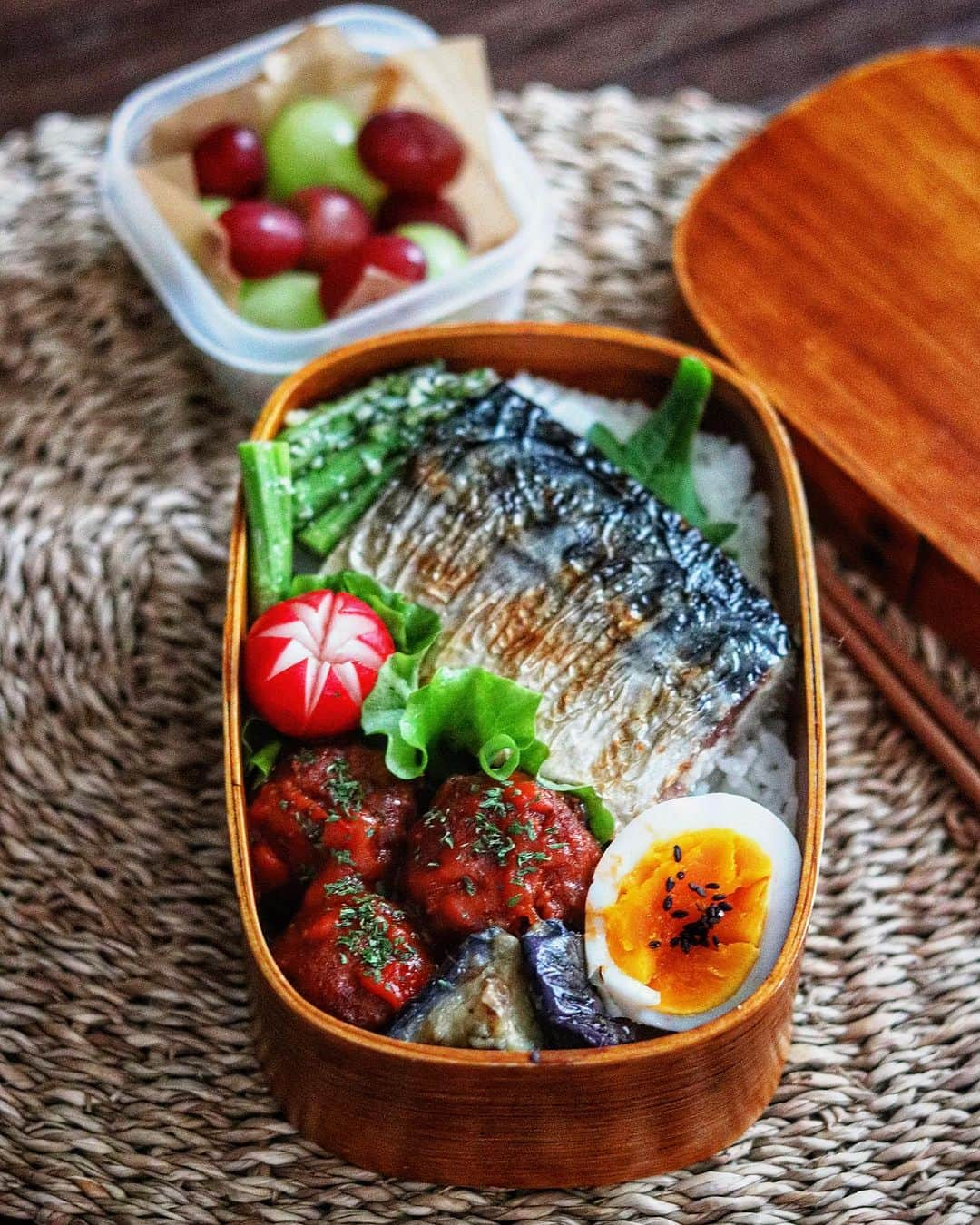 奥田和美のインスタグラム：「今日は和洋な高校生男子弁当🍱  ✳️焼き塩サバ ✳️トマトソース肉団子 ✳️茄子の麺つゆおかか ✳️アスパラチーズ ✳️ゆで卵 ✳️ぶどう  サバ大好きなので、今日は焼き鯖入ってるよと言ったらちょっとウキウキしていました、可愛い奴やな😆  茄子は作りおきの素揚げに麺つゆかけてチン、かつお節をまぶしています。 素揚げしてあるので、時間が経って既にトロトロ！ 再加熱程度の時間で煮込んだような柔らかさ🍆  アスパラはオリーブオイルかけてチン、粉チーズで和えてます。  ラディッシュは前日の夜にはちみつレモンに漬けておきました🍋  ちなみにトマトソース肉団子は冷凍食品🍅 湯煎温めだったので、湯煎のお湯に卵も一緒に入れてゆで卵作りました🥚  朝は鯖焼いただけ🐟  今日はのり弁潜んでません、ごめんよ次男。（昨日は突如現れたのり弁めっちゃ嬉しかったらしい）  今日のお弁当どうだった？って聞くと 「めっっっっちゃ旨かったわ、ありがとう」 と言ってくれる次男、ほんまええ奴や…😭  #高校生男子弁当  #男子弁当  #わっぱ弁当箱  #わっぱ弁当  #焼き鯖弁当  #焼き鯖  #塩焼き鯖弁当  #トマトソース  #肉団子  #トマトソース肉団子」