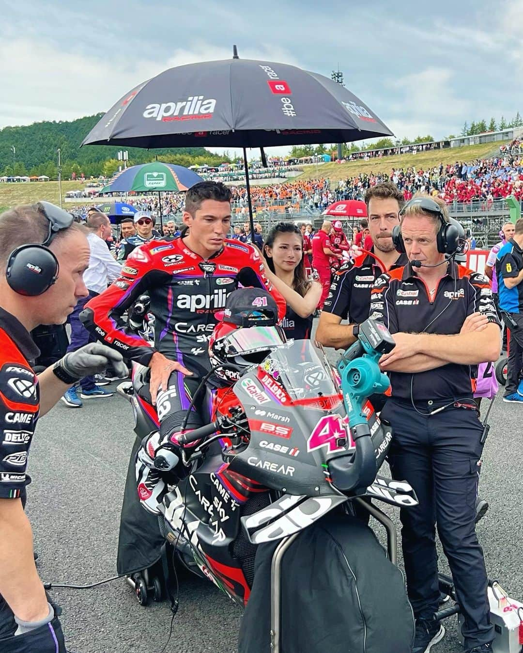 葉月美優のインスタグラム：「❥今日はMotoGP日本グランプリ2023 決勝レース日でした！  長くなるので今日はレースの話のみです🙏🏻  aprilia RACINGのアンブレラガールとして、PIT WALKやグリッドに立たせていただきました。そして、アレイシ・エスパルガロ選手の担当でした💕  昨日はスプリントレースでも立たせていただきました！ アレイシ選手はドリンクをよくドリンクを飲みますが、最後エンジン始動時にクルーではなく横にいる私にドリンクを渡されて、「あ！私なのか」と少し笑えてしまいました🤭そのままPITへ持っていき返却◎  今日も同じく私に渡されましたが、その時に目を見てニコッとしてくれて、ドキッとしました(˶‎° °‎˶)♡ これはキラーだ！！！　  aprilia RACINGのお2人、アレイシ選手とビニャーレス選手は神対応ですからね〜✨  さて決勝レースですが、  オープニングセレモニー中に、パラパラ雨が降ってきました。タイヤは全ライダースリック。スタートしてすぐ、ホワイトフラッグでバイクの乗り換えがOKとなりました。  スタート直後、#12 ビニャーレス選手は、1コーナーで他の車両に押し出され、もう1台と接触し転倒してしまい、復帰後は下位を走行。  #41 アレイシ選手は勢いがよく、9番手から4番手に！　1周でレインタイヤに交換し7番手でPIT OUT後、2番手まで追い上げ！  1番手はまだスリックタイヤだったので裏の1番手ですね♫　そして1番手車両がPIT inし、アレイシ選手がコース上の1番手に✨  この時点で残り19周…何が起こるかわからない。早く終われ〜という気持ちでいっぱい（笑）  しかしここから雨が強まり、 GAPは0.3、0.5、0.4…とドキドキが止まらない中、後退していた#89 がどんどん上位を抜いてきてついに、2番手まで迫られ…ヘアピンの立ち上がりから90度のブレーキングで、抜かれてしまいます。  その後は、次々と抜かれて6番手まで後退。5番手まで取り戻しますが、土砂降りにより残り12周で赤旗中断。  5番グリッドからの再開後、やはりレースができる状況ではなく1周目で赤旗終了。  #41 アレイシ選手は5位、#12 ビニャーレス選手は19位となりました🏁  厳しい状況のレースでしたね。こんな中でも、私が見たときは平均速度は143Km/hほど、最高速は300km/hほどと、さすがMotoGPライダーですね。  私は雨じゃ走らないと言って、何度怒られてきたことかʅ( ᷄ω ᷅ )ʃ  ずっと目が離せずPITから見ていたので、バイクのチェンジも目の前で見ることができました！なんてかっこいいの！？　めちゃ早だし、クルーのサポートもさすがすぎました。  赤旗中断中も色々見ましたが、詳しくはwebオートバイに書いたので読んでください🥺かなり長いので覚悟してね（笑になることもって、間近で見れて感動のtoGPでした！  #aprilia #apriliaracing #apriliajapan #アプリリア #アプリリアレーシング #motogp #motogp2023 #motogpjapan #motogp日本グランプリ #bikerace #bikegirl #umbrellagirl #racequeen #バイク女子 #レースクイーン #アンブレラガール #大型バイク女子 #サーキット女子 #バイクファッション #アレイシエスパルガロ #マーベリックビニャーレス #aleixespargaro #maverickvinales #バイク女子フォト #バイクレース #モビリティリゾートもてぎ #rsv4」