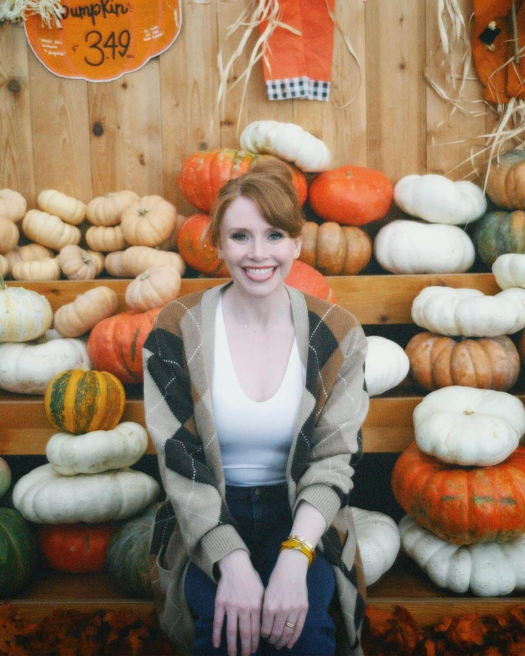 ブライス・ダラス・ハワードのインスタグラム：「Hey, October 😉🍂⁣⁣ ⁣⁣ 📸: @andiejjane⁣⁣ ⁣⁣ [ID: BDH playfully poses in front of a display at @traderjoes with pumpkins of all different shapes, sizes, and colors. In full autumn vibes, she wears navy blue jeans, a white t-shirt, and a beige and brown cardigan. 3 smiling scarecrows hang on the wall in the back.]⁣」