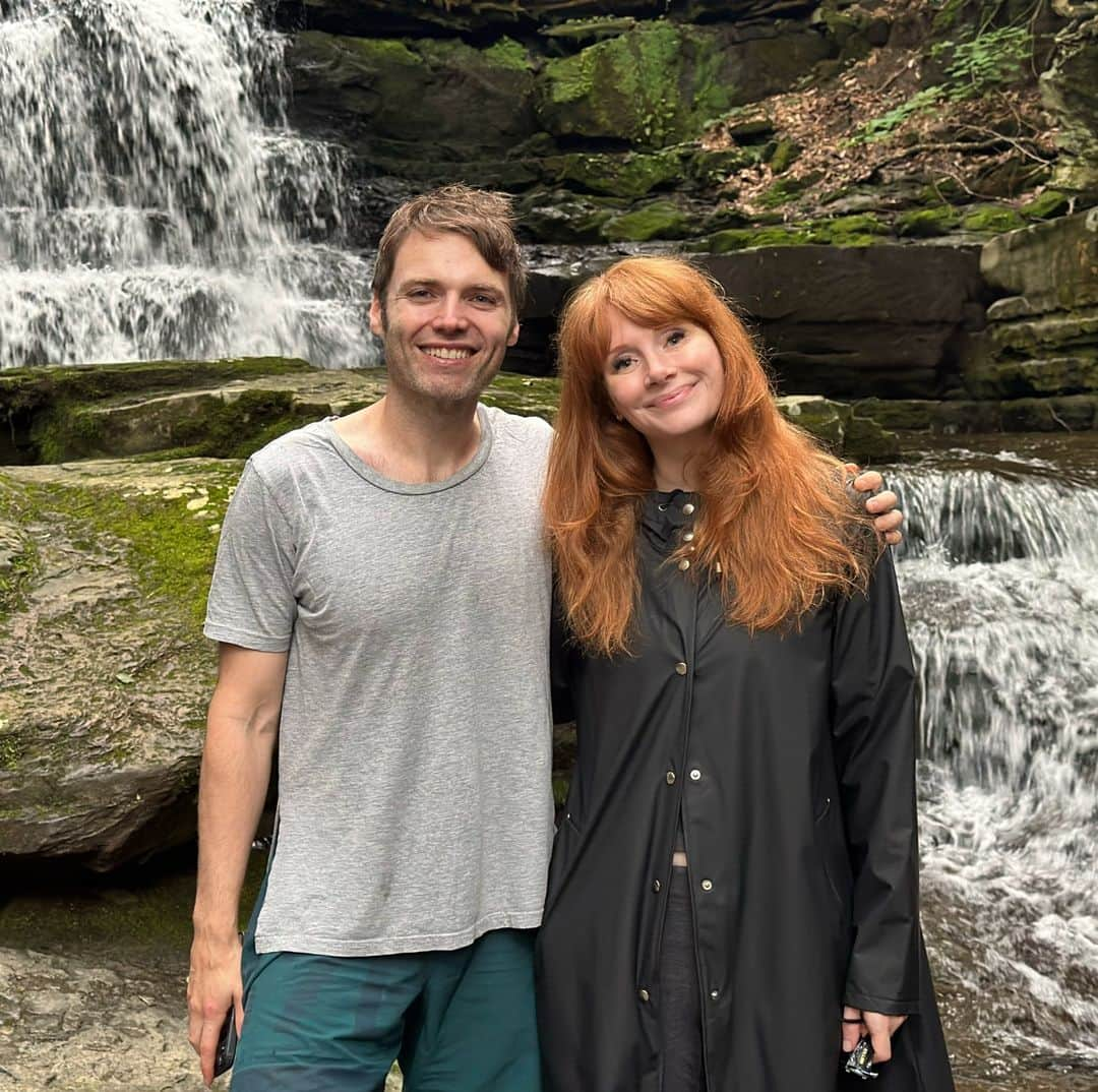 ブライス・ダラス・ハワードのインスタグラム：「Happy Birthday handsome, I love you so much! @stealthgabel  [ID: Standing in front of a rushing waterfall and mossy rocks in rural Pennsylvania, Seth Gabel (left) and BDH (right) wrap their arms around each other for a photo. Seth wears a grey t-shirt and teal swim trunks and BDH wears a black long raincoat and her hair down.]」