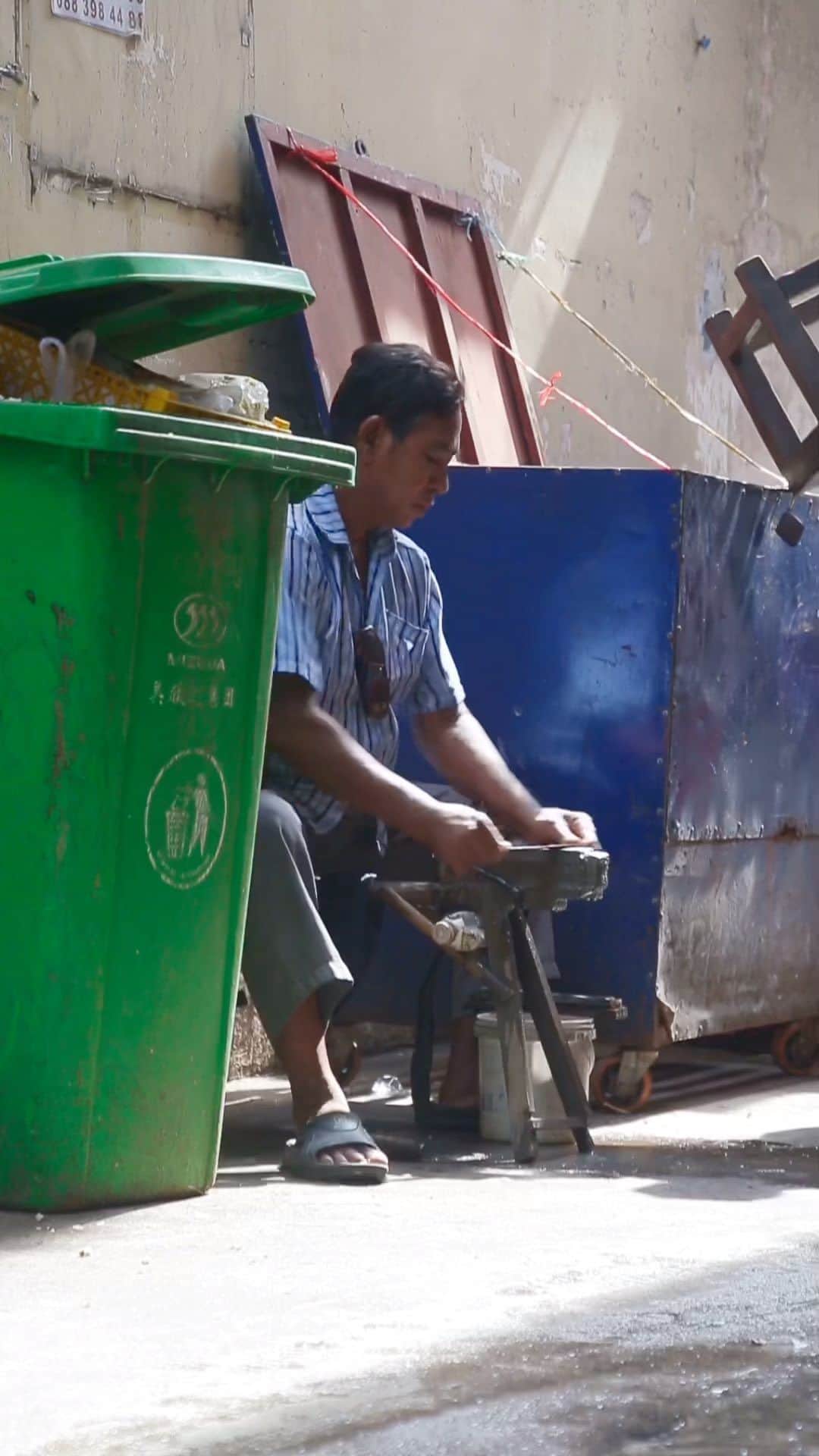 Shunsuke Miyatakeのインスタグラム：「Cutlery sharpener /   There are many kinds of work to be found on the streets of Phnom Penh. A cutlery sharpener is one of them. In a corner of downtown Phnom Penh that I often visit, there is a cutlery sharpener who always works at the same place. It is always between a garbage can and a box for storing stall chairs.  He has an air of craftsmanship that makes it difficult to get to know him, but as I pass by more and more times, he allows me to approach him and take a video of him.  The morning light shines through the buildings, illuminating the craftsmen's work. It is divine.」