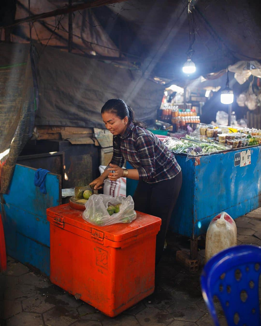 Shunsuke Miyatakeさんのインスタグラム写真 - (Shunsuke MiyatakeInstagram)「Woman cutting lime while chatting / Kep, Cambodia  The crab market in Kep attracts many tourists. The crabs are pulled out of the water and boiled in front of them, and tourists are happy to buy them.  Light shines through a hole in the ceiling of the market onto the smoke from the charcoal burning to boil the crabs.  The lime juice of a woman cutting limes deftly as she chatted with her friend was also a treat.  #PhnomPenhPhotographyCollective」9月13日 20時19分 - casadetake