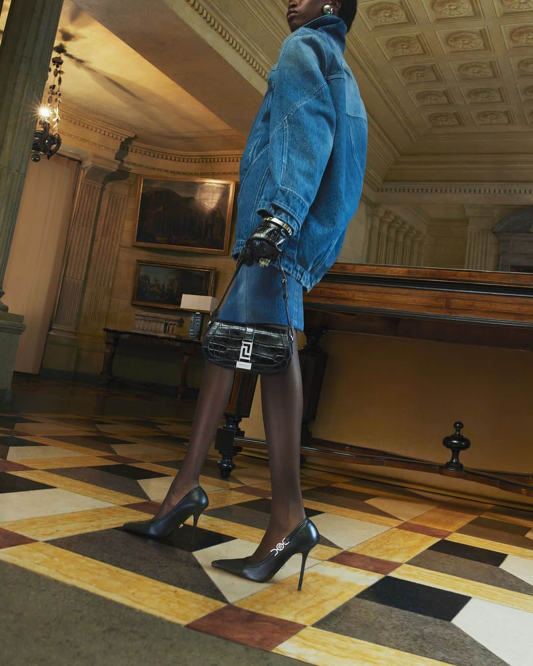 ジャンニヴェルサーチのインスタグラム：「Fall-Winter 2023 Campaign  Model wears denim cocoon parka; denim pencil skirt; croc-embossed leather gloves; Medusa '95 slingback pumps; Greca Goddess mini bag  Photography by Mert & Marcus  #VersaceFW23 #VersaceGrecaGoddess」