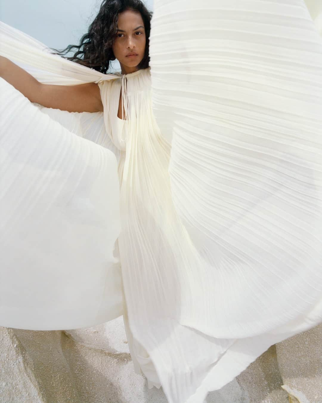 Chloéのインスタグラム：「The pleats and gathers of the cape and long dress in lower-impact wool gauze unfurl like the rays of Alectrona – the greek goddess of the sun.   The #ChloeAW23 campaign was shot by @zoeghertner at Sarakiniko on Milos island in Greece.   Creative director: @gabrielahearst Art director: #PeterMiles Stylist: #CamillaNickerson Models: @devynfaithgarcia」