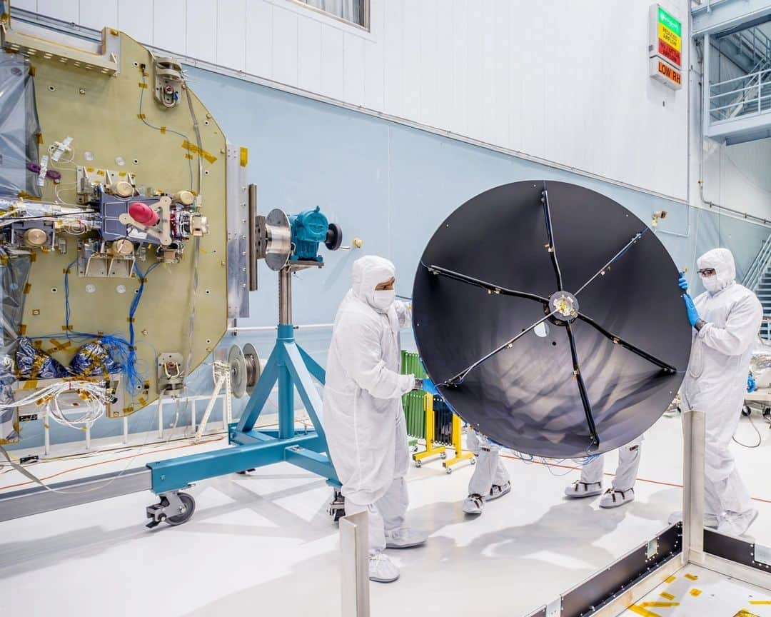 NASAのインスタグラム：「What’s the dish! #ICYMI The Nancy Grace Roman Space Telescope's high-gain antenna system has been integrated onto the spacecraft’s communications panel in the Goddard clean room. The antenna will be able to send status updates of the spacecraft back to Earth, as well as up to 500 megabytes per second of data to ground systems across three different continents!   Photo Credit: NASA/ Chris Gunn  Image Description:  1: Wide shot inside the Goddard cleanroom. Two people in white head-to-toe suits with face coverings are holding a large black antenna dish. There are two people standing behind the dish but only their feet are visible.  To the left, there is a large gold round panel that is supported on a blue and grey stand. There is a silver beam that is laying flesh on the panel. 2: Side view of a large round black antenna dish in the foreground. There is blue wiring lining the outside of the dish. In the background is a large round panel standing upright. The panel is half gold and half white. There are square and rectangular boxes fused to the panel. There are two people standing in front of the panel in a white head-to-toe suit. They are examining one of the boxes on the panel.  3:Top view of the Roman communications panel, it is a large round and flat panel that is half gold and half white. There are small gold boxes welded to the panel.  There is a large black round antenna dish sitting on the gold side of the panel.  There is a person in a white head-to-toe suit and face covering to the top right of the panel. They have on blue gloves and are pointing at a wire that is attached to the panel.」