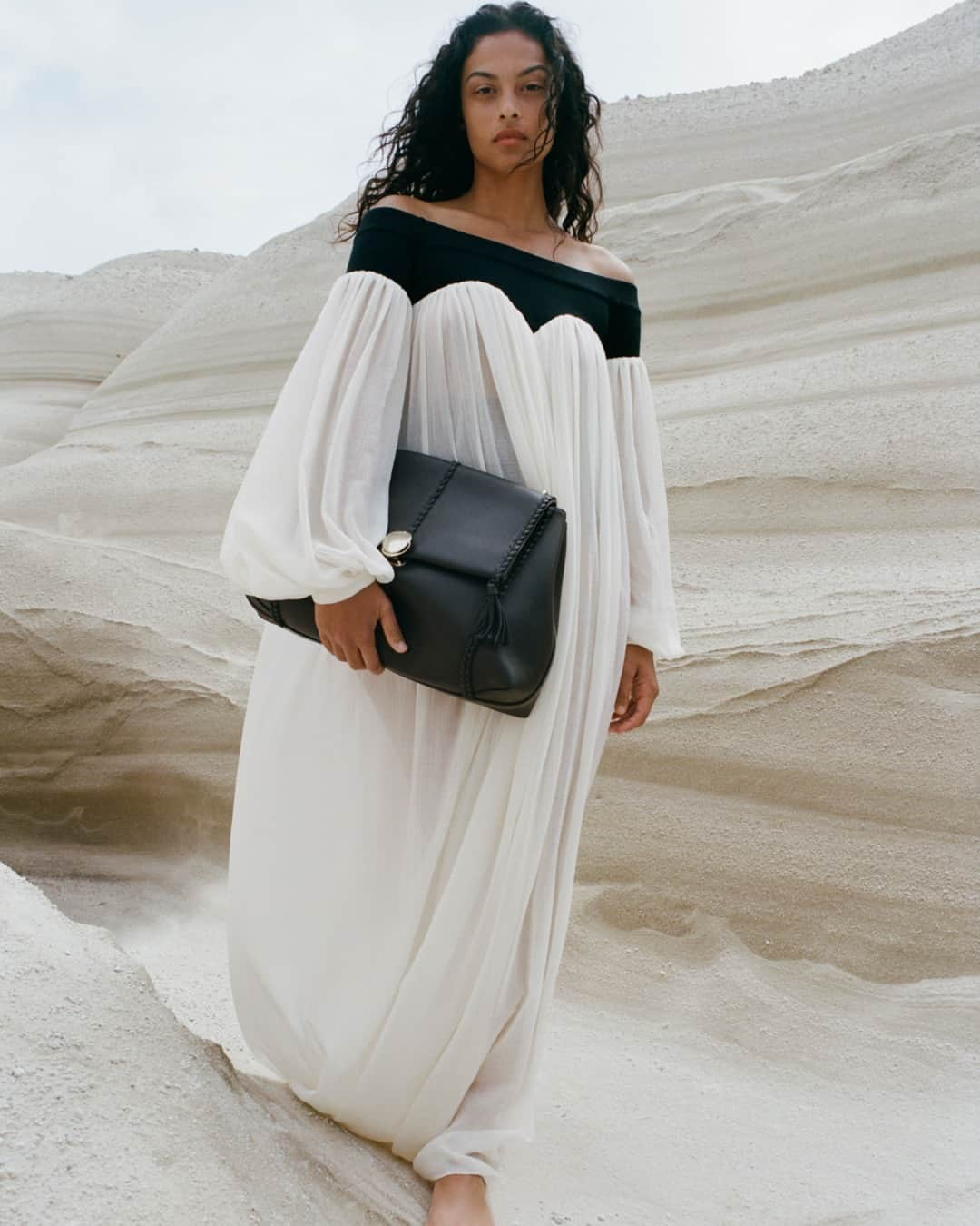 Chloéのインスタグラム：「The flowing lines of the maxi dress in lower-impact wool gauze and Penelope shoulder bag are captured in harmony with the volcanic rock strata of Sarakiniko on Milos Island, Greece.   #ChloeAW23  Creative director: @gabrielahearst Art director: #PeterMiles Photographer: @zoeghertner Stylist: #CamillaNickerson Models: @devynfaithgarcia」