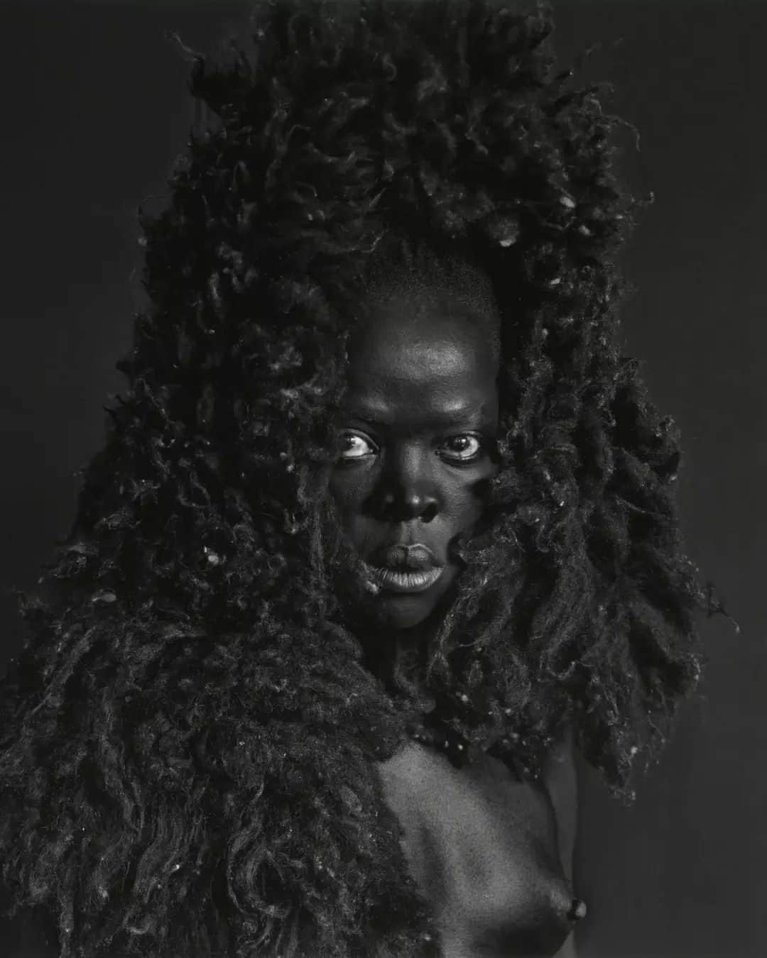 のインスタグラム：「'I use art as my own means of articulation. It heals.’ - @muholizanele 🖤   From the early 2000s, #ZaneleMuholi has documented and celebrated the lives of South Africa’s Black lesbian, gay, trans, queer and intersex communities. Muholi turns the camera on themself in their ongoing series, titled 'Somnyama Ngonyama' ('Hail the Dark Lioness' in Zulu), made up of powerful self-portraits taken around the world. These striking black and white portraits use everyday household objects like sunglasses and wire sponges to create elaborate clothing and hair pieces.   The artist described their 'Somnyama Ngonyama' series as 'an unflinchingly personal approach I have taken as a visual activist to confronting the politics of race and pigment in the photographic archive. It is a statement of self-presentation through portraiture.'  Catch Muholi's solo exhibition at Tate Modern next summer. ✨   📸 Somnyama IV, Oslo 2015 📸 Bona, Charlottesville 2015 📸 Thembeka I, New York, Upstate 2015」