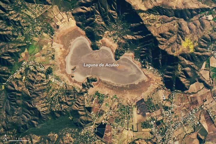 NASAのインスタグラム：「Laguna de Aculeo is no longer parched! NASA satellites began to detect water in August, after an intense winter storm dropped as much as 15 inches of rain. These images show the lake on May 18 and in early September.  Image descriptions:  Image 1: Landsat 9 image from May 18, 2023. A dry lakebed creates an irregular kidney shape in the center of the image, with darker and lighter rings extending out from it. The area around the lakebed is mottled greens and browns.  Image 2: The same area in a Landsat 9 image from September 7, 2023, following heavy rains. In this image, the lake has been halfway filled; the lake itself appears swirls of blues and greens. The area around the lake is almost entirely green, surrounded by healthy vegetation.」