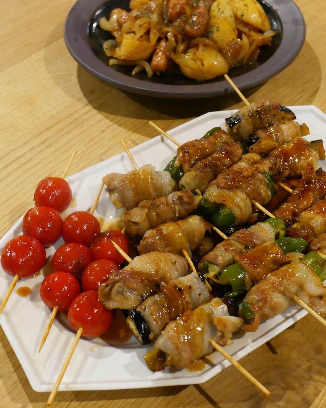 のインスタグラム：「おうちで串刺し豚巻き作った日です☺️  豚バラ肉で、野菜室にて油を売っていた野菜たちを引っ張り出して豚バラに包まれてもらいました。  ピーマンにはチーズをさらに包んで🧀  ミニトマトは何にも包まれずただの威張り🍅になってしまいました。  タレは、お酒みりん醤油アガベシロップで😍  私は甘いタレが好きなので、みりんたっぷりにしてしまう習性があるのですが、辛みがお好きならば、七味を最後に振りかけたら素敵です💓  串にすれば不思議とお米なくても脳をごまかせるのでいいです。  あとはジャガイモとウインナーでの味炒めです🥔  秋だからか、夜もしっかりお腹すくようになってしまいました。  気をつけるべきは、はやい夜ご飯を☺️です。」