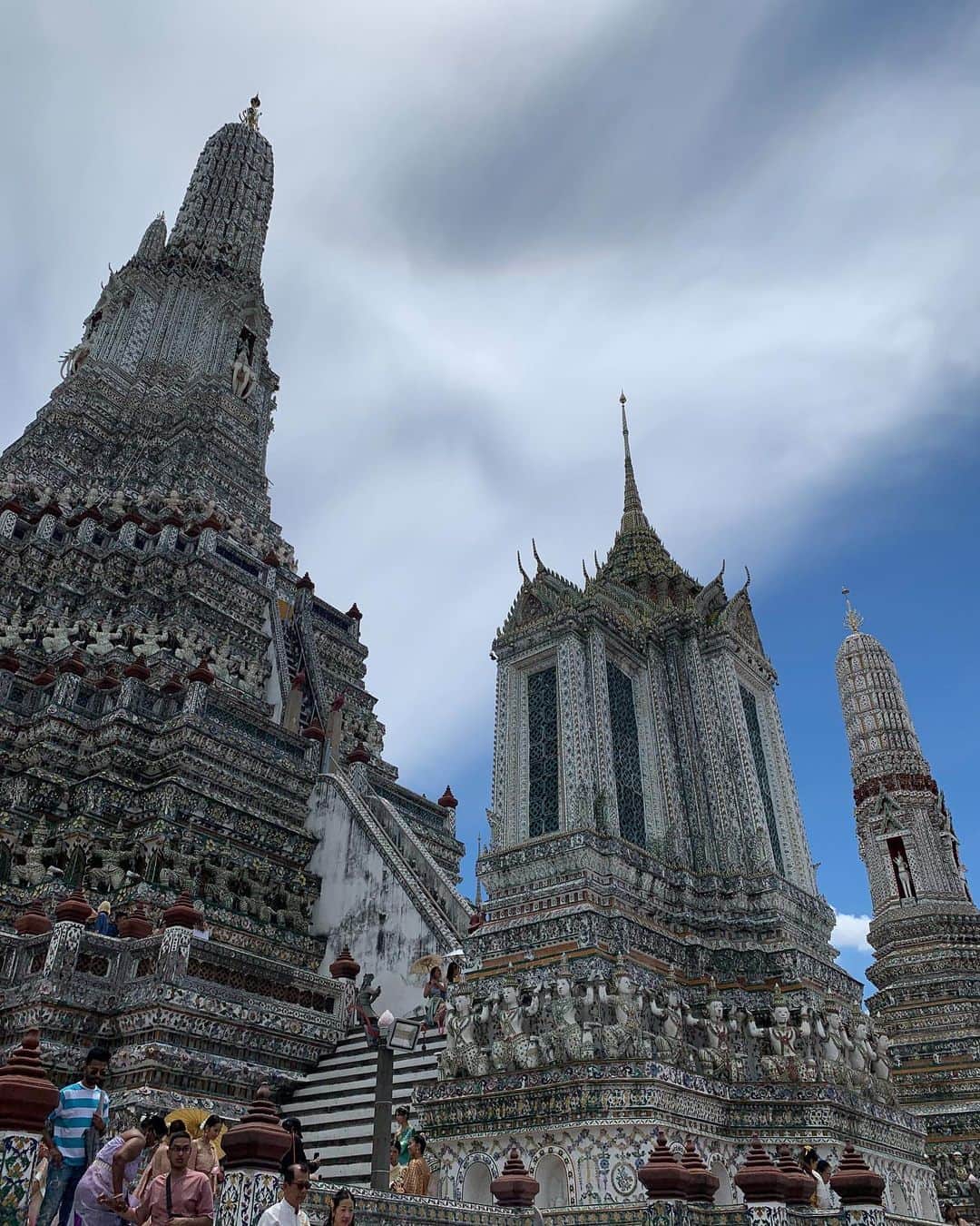 職人.comさんのインスタグラム写真 - (職人.comInstagram)「【ワット・アルンと名物アイス】  夏の終わりに、タイの首都バンコクへ初めて行ってきました。一般的に6月～10月のタイは雨季といわれていますが、滞在中はラッキーなことにほとんど晴れていました。国民の約95%が仏教徒である仏教国タイにはさまざまな寺院があり、黄金に輝くきらびやかな寺院や像、装飾などを街のあちこちで目にします。その中で、バンコク三大寺院の一つであるワット・アルンは少し雰囲気が異なっていて、タイについて下調べをしていたときからここは実際に訪れて自分の目で見てみたいと思っていました。  「ワット・アルン」（正式名称：ワット・アルン・ラーチャワララーム）は、アユタヤ時代に建立されたバンコクのチャオプラヤー川沿いにある仏教寺院。ワット・アルンとは「暁の寺」という意味で、三島由紀夫が書いた小説のタイトルにもなっています。タイの硬貨、10バーツにも描かれ、世界中から訪れる観光客、そしてタイ国民から愛され続けている寺院です。朝、昼、夜でまったく違う表情を見せてくれるのもワット・アルンの魅力で、その名のとおり、朝焼けに染まる姿や夕日を背にしたシルエットはとても美しく、日中は日の光を反射して輝き、夜にはライトアップされます。  ワット・アルンへの行き方は、対岸のターティアン船着場から渡し船で向かう方法がポピュラーです。日本円にして数十円程度で、ワット・アルンをはじめとしたタイの景色を楽しみながらチャオプラヤー川を渡ることができます。  船から降りて目の前にそびえ立つのは、この色とりどりの5基の仏塔。大仏塔の高さは75メートル、台座の周囲は234メートルもあり、ヒンドゥー教の聖地カイサーラ山をかたどっているといわれています。仏塔の表面には無数の陶片が埋め込まれており、遠くから眺めていた印象とはまた違った美しさ。実際に仏塔の上に登って間近で見て回ることができるため、ぜひ一周して一つ一つの模様や形、配置、色を見比べてみてほしいのですが、階段が非常に急なのです。タイの民族衣装を着て写真撮影をしている観光客を多く見かけたのですが、あの衣装でこの階段を上り下りするガッツは尊敬に値します。階段では転がり落ちないよう、くれぐれもお気をつけください。それも含めて、探検気分を楽しめてエキサイティングな体験でした。  ワット・アルンを歩き回り一汗かいたあとは、敷地内にある「アルン・カフェ」という売店のような小さなカフェへ。こちらには、ワット・アルンの装飾タイルを模したアイスが売られています。このかわいい見た目を侮るなかれ、実際に頼んでアイスを目の前にした時、模様の緻密さや凹凸、周りを囲む4つの花がすべて異なっているデザイン性の高さなどに驚きました。アイスなのに美術品のよう。眼福です。もったいないですが、溶ける前に食べなければいけません。味は、オレンジのタイティーと青のバタフライピーの2種類。どちらもタイで愛されているお茶で、味からもしっかりとタイを感じられるのも嬉しいところ。アイスや飲み物を片手に、ベンチに腰掛けてゆっくりする人々でカフェの周りはにぎわっていました。このアイスは今年の5月から販売開始したようなのですが、こうして歴史的建造物の模様やイメージなどをデザインに落とし込み、更に多くの人に興味を持ってもらうきっかけにするというのは、この先その場所を残していくうえでとても良い方法だと感じました。  帰国して写真を見返していて、綺麗だった、行って良かったと改めて思うお寺だったため、タイに行かれる際はぜひおすすめしたい場所です。  ワット・アルン（暁の寺） https://goo.gl/maps/Z9fUn5pwP9iTDgXb6 アルン・カフェ https://goo.gl/maps/dJ1ERjfiFd3p5UxE6  参考資料 https://www.thailandtravel.or.jp/wat-arun/ https://www.arukikata.co.jp/web/article/item/2210744/ https://www.bangkoknavi.com/miru/40/ https://www.tokyo-np.co.jp/article/265121  @shokunincom  #職人ドットコム #京都市 #上京区 #中京区 #西陣 #キッチン用品 #調理道具 #調理器具 #料理道具 #台所道具 #手仕事 #暮らしの道具 #暮らしを楽しむ #工芸品 #民芸 #民藝 #器のある暮らし #焼き物 #生活工芸 #ワットアルン #ワットアルンラーチャワララーム #名物アイス #眼福 #暁の寺 #アルンカフェ #仏塔 #タイ観光 #バンコク #タイ名所 #タイのお寺」9月27日 14時52分 - shokunincom