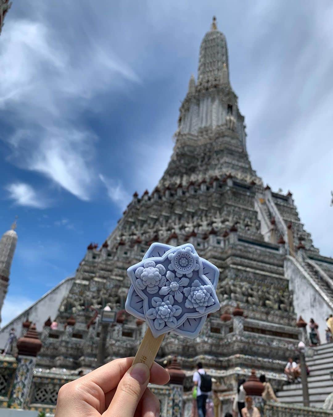 職人.comさんのインスタグラム写真 - (職人.comInstagram)「【ワット・アルンと名物アイス】  夏の終わりに、タイの首都バンコクへ初めて行ってきました。一般的に6月～10月のタイは雨季といわれていますが、滞在中はラッキーなことにほとんど晴れていました。国民の約95%が仏教徒である仏教国タイにはさまざまな寺院があり、黄金に輝くきらびやかな寺院や像、装飾などを街のあちこちで目にします。その中で、バンコク三大寺院の一つであるワット・アルンは少し雰囲気が異なっていて、タイについて下調べをしていたときからここは実際に訪れて自分の目で見てみたいと思っていました。  「ワット・アルン」（正式名称：ワット・アルン・ラーチャワララーム）は、アユタヤ時代に建立されたバンコクのチャオプラヤー川沿いにある仏教寺院。ワット・アルンとは「暁の寺」という意味で、三島由紀夫が書いた小説のタイトルにもなっています。タイの硬貨、10バーツにも描かれ、世界中から訪れる観光客、そしてタイ国民から愛され続けている寺院です。朝、昼、夜でまったく違う表情を見せてくれるのもワット・アルンの魅力で、その名のとおり、朝焼けに染まる姿や夕日を背にしたシルエットはとても美しく、日中は日の光を反射して輝き、夜にはライトアップされます。  ワット・アルンへの行き方は、対岸のターティアン船着場から渡し船で向かう方法がポピュラーです。日本円にして数十円程度で、ワット・アルンをはじめとしたタイの景色を楽しみながらチャオプラヤー川を渡ることができます。  船から降りて目の前にそびえ立つのは、この色とりどりの5基の仏塔。大仏塔の高さは75メートル、台座の周囲は234メートルもあり、ヒンドゥー教の聖地カイサーラ山をかたどっているといわれています。仏塔の表面には無数の陶片が埋め込まれており、遠くから眺めていた印象とはまた違った美しさ。実際に仏塔の上に登って間近で見て回ることができるため、ぜひ一周して一つ一つの模様や形、配置、色を見比べてみてほしいのですが、階段が非常に急なのです。タイの民族衣装を着て写真撮影をしている観光客を多く見かけたのですが、あの衣装でこの階段を上り下りするガッツは尊敬に値します。階段では転がり落ちないよう、くれぐれもお気をつけください。それも含めて、探検気分を楽しめてエキサイティングな体験でした。  ワット・アルンを歩き回り一汗かいたあとは、敷地内にある「アルン・カフェ」という売店のような小さなカフェへ。こちらには、ワット・アルンの装飾タイルを模したアイスが売られています。このかわいい見た目を侮るなかれ、実際に頼んでアイスを目の前にした時、模様の緻密さや凹凸、周りを囲む4つの花がすべて異なっているデザイン性の高さなどに驚きました。アイスなのに美術品のよう。眼福です。もったいないですが、溶ける前に食べなければいけません。味は、オレンジのタイティーと青のバタフライピーの2種類。どちらもタイで愛されているお茶で、味からもしっかりとタイを感じられるのも嬉しいところ。アイスや飲み物を片手に、ベンチに腰掛けてゆっくりする人々でカフェの周りはにぎわっていました。このアイスは今年の5月から販売開始したようなのですが、こうして歴史的建造物の模様やイメージなどをデザインに落とし込み、更に多くの人に興味を持ってもらうきっかけにするというのは、この先その場所を残していくうえでとても良い方法だと感じました。  帰国して写真を見返していて、綺麗だった、行って良かったと改めて思うお寺だったため、タイに行かれる際はぜひおすすめしたい場所です。  ワット・アルン（暁の寺） https://goo.gl/maps/Z9fUn5pwP9iTDgXb6 アルン・カフェ https://goo.gl/maps/dJ1ERjfiFd3p5UxE6  参考資料 https://www.thailandtravel.or.jp/wat-arun/ https://www.arukikata.co.jp/web/article/item/2210744/ https://www.bangkoknavi.com/miru/40/ https://www.tokyo-np.co.jp/article/265121  @shokunincom  #職人ドットコム #京都市 #上京区 #中京区 #西陣 #キッチン用品 #調理道具 #調理器具 #料理道具 #台所道具 #手仕事 #暮らしの道具 #暮らしを楽しむ #工芸品 #民芸 #民藝 #器のある暮らし #焼き物 #生活工芸 #ワットアルン #ワットアルンラーチャワララーム #名物アイス #眼福 #暁の寺 #アルンカフェ #仏塔 #タイ観光 #バンコク #タイ名所 #タイのお寺」9月27日 14時52分 - shokunincom
