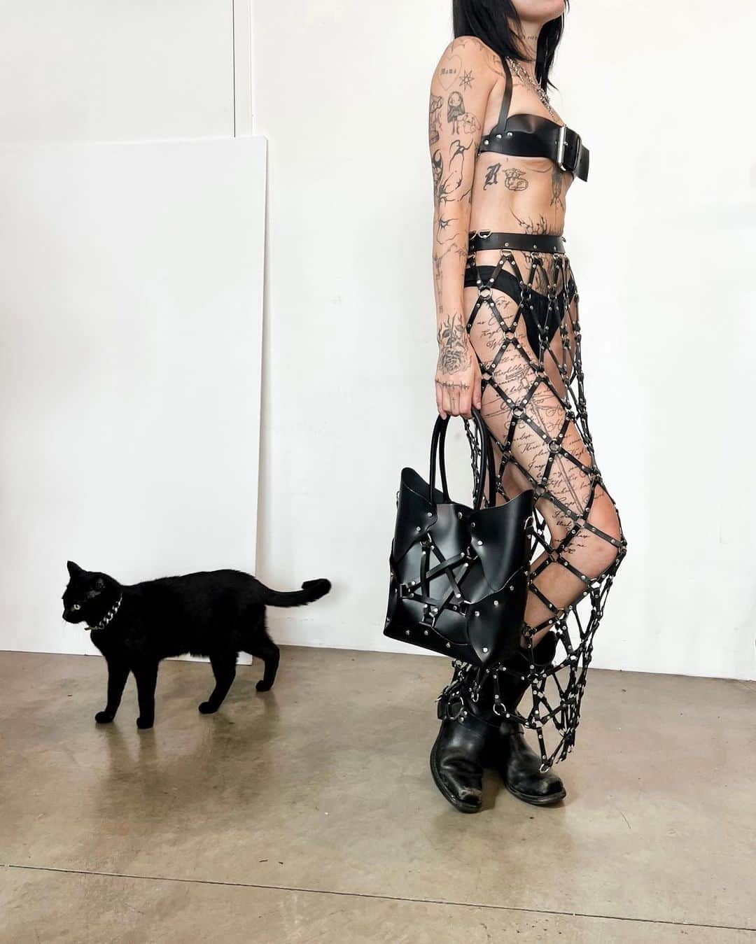 ZANA BAYNEのインスタグラム：「Romy and Puppy 🐈‍⬛  @deathbyromy wears the Halter Buckle Bra, Linked Column Skirt (price upon request), and Pentagram Handbag all in Black Leather」